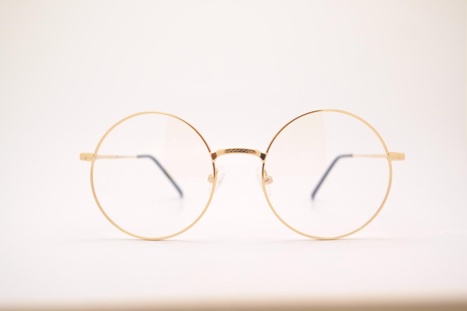 Gold round eyeglasses with clear lenses and black temple tips on a white background.