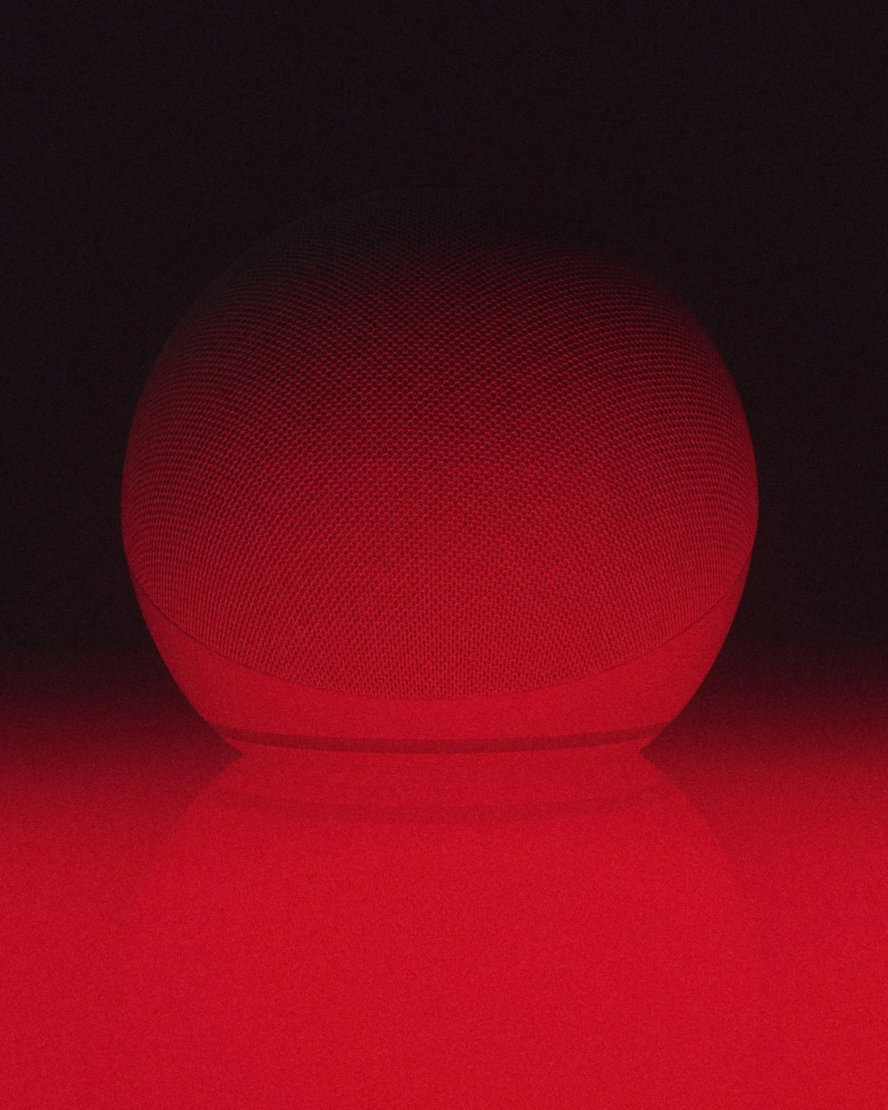 Red smart speaker glowing in a dark environment with a red light reflection on the surface below.