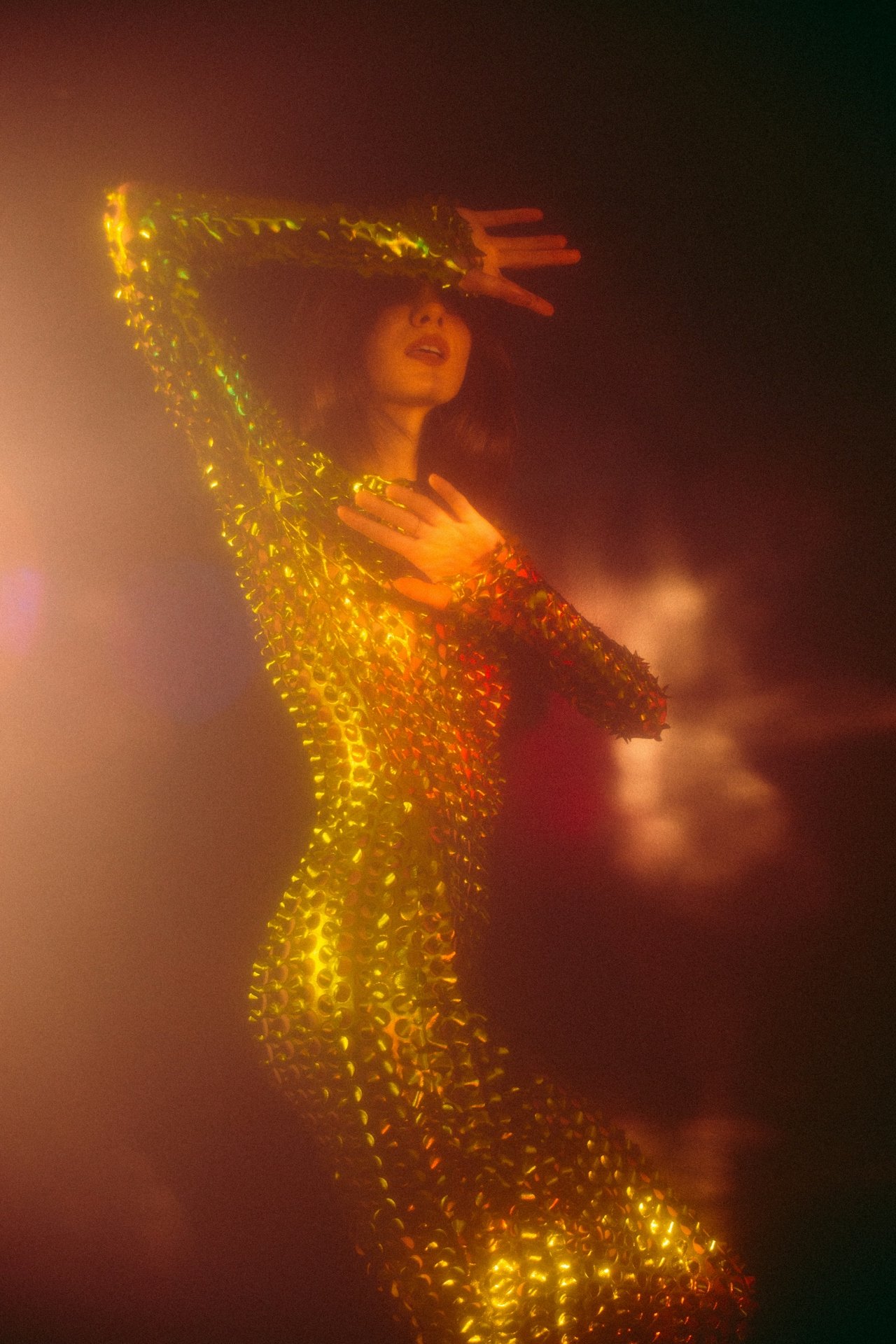 Woman performing on stage, wearing a shiny, gold outfit with a matching headpiece, illuminated by warm stage lighting.