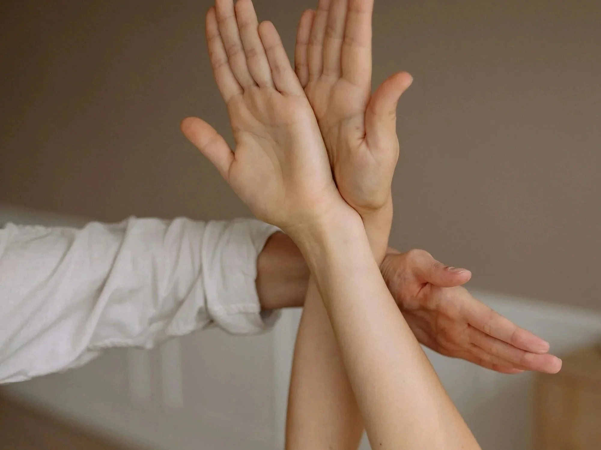 Two pairs of human hands touching, one pair on top of the other, against a plain background.