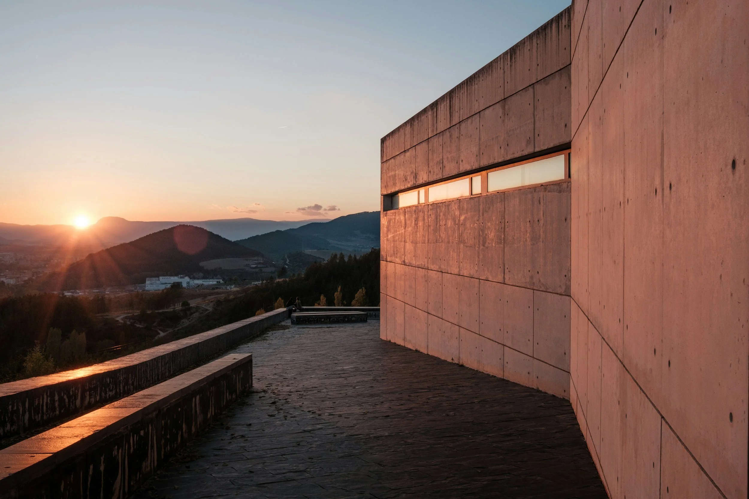 Modern concrete building with rectangular windows at sunset overlooking mountains.