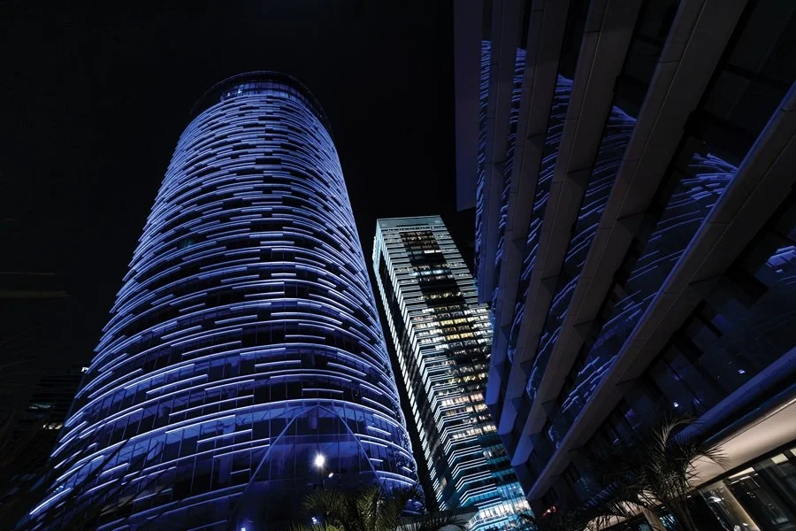 Edificios modernos en una ciudad durante la noche, con luces azules y ventanas iluminadas.