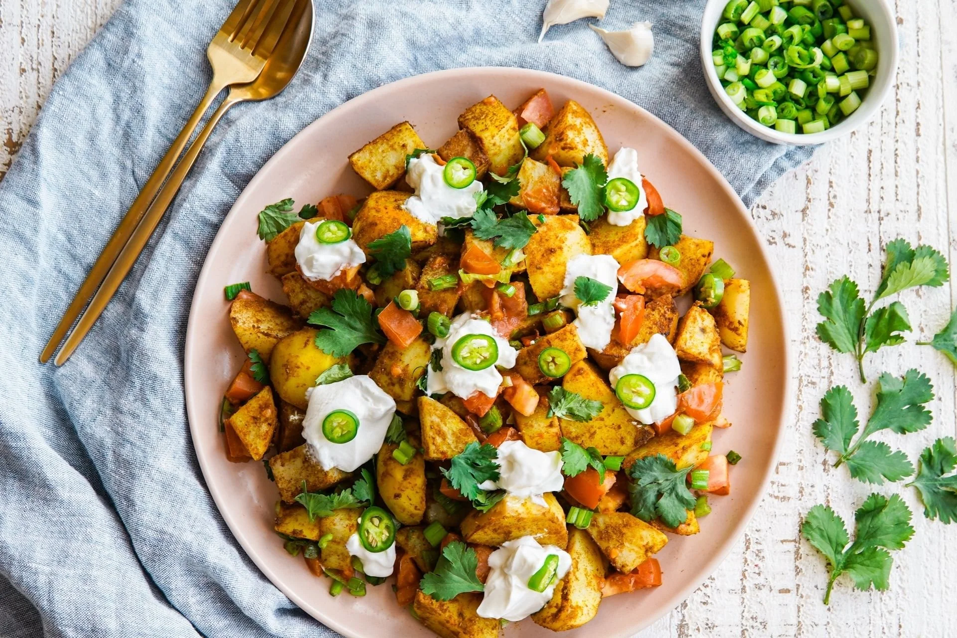 Bombay potatoes with spiced golden potato chunks, fresh tomato, green chilli, coriander and dollops of yoghurt, topped with sliced spring onion.