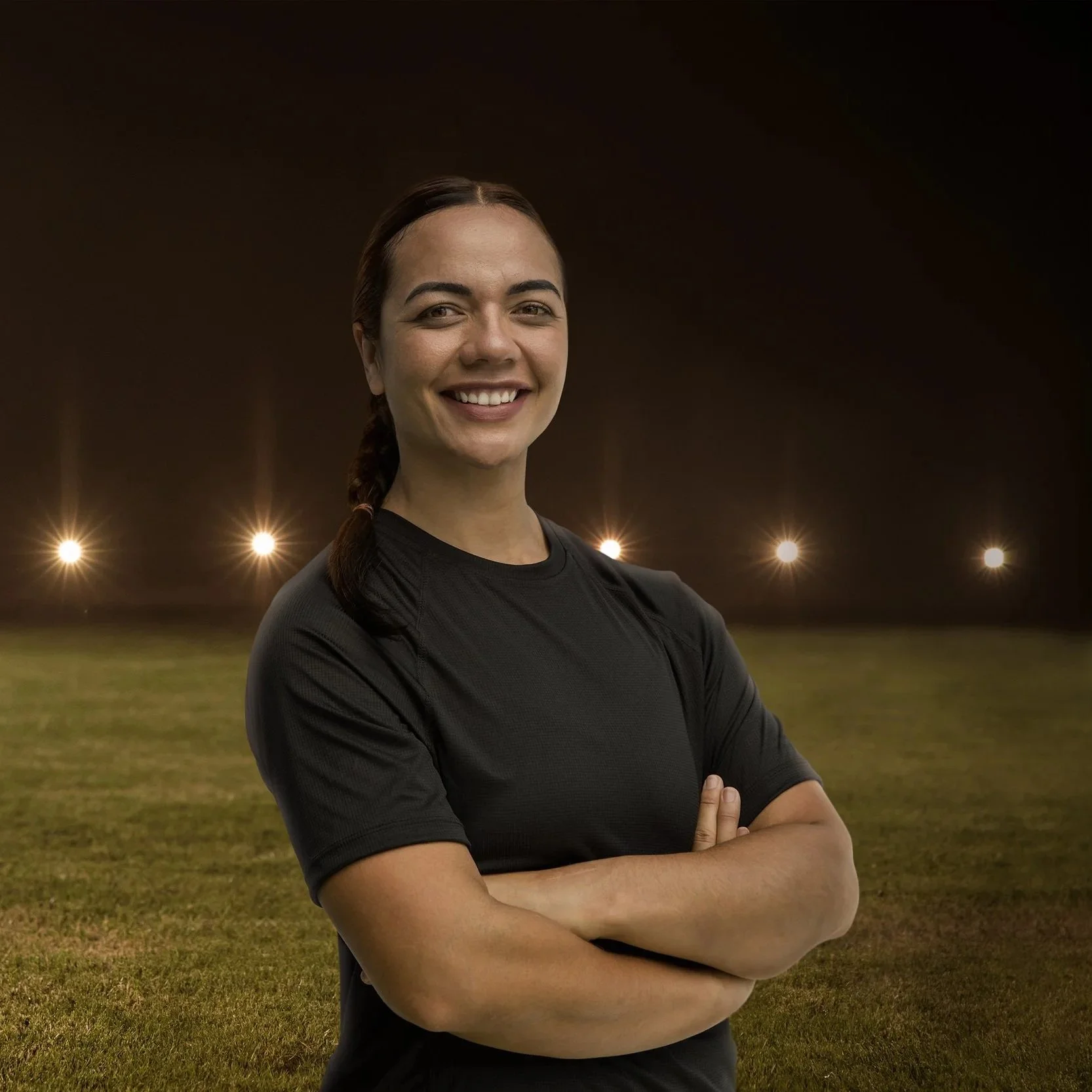 Beef + Lamb New Zealand ambassador Stacey Waaka smiling with arms crossed on a floodlit rugby field