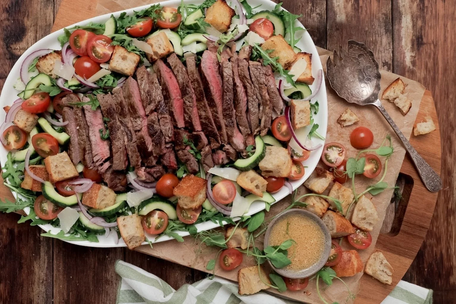 Sliced grilled steak served over a fresh salad of rocket, cucumber, cherry tomatoes, red onion, shaved parmesan and golden croutons, with dressing on the side.