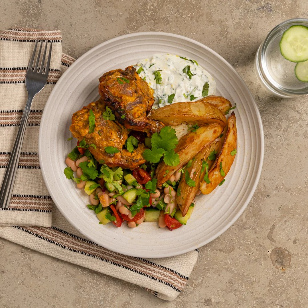 Tandoori lamb chops served with golden potato wedges, a fresh cucumber, tomato and white bean salad, creamy herb yoghurt sauce and fresh coriander.