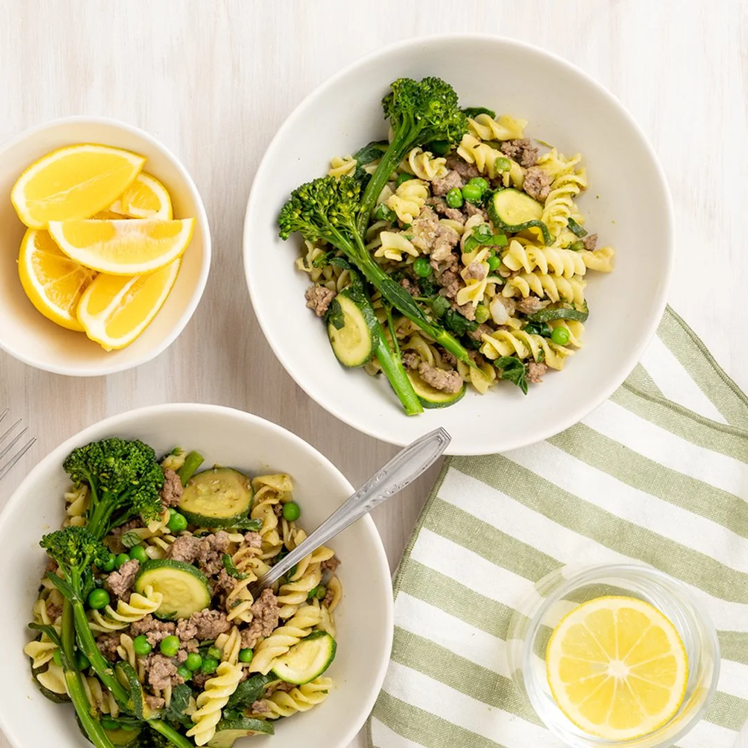 Lamb mince and pesto pasta with courgette, peas, broccolini and fresh greens, served with lemon wedges.
