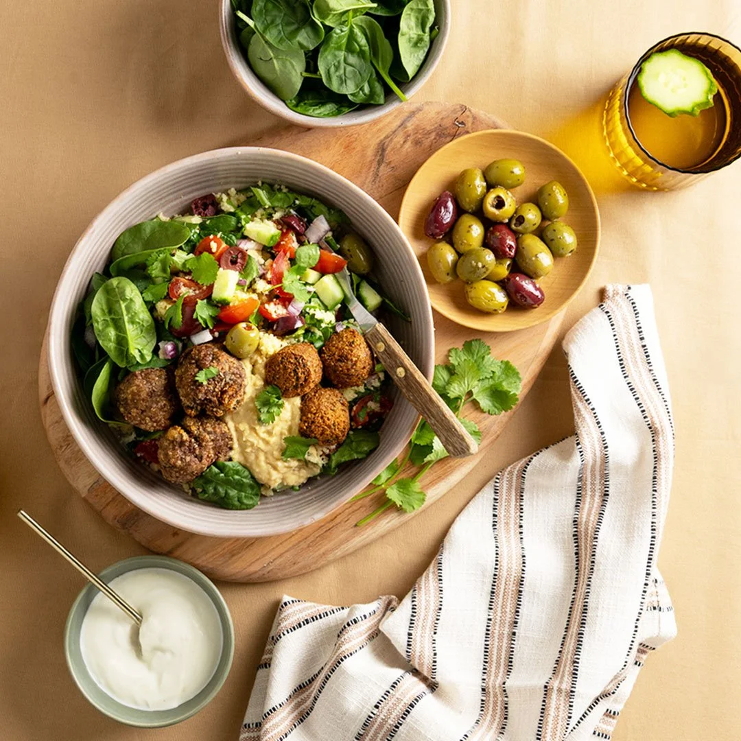 Air fryer beef meatballs and falafel served in a Mediterranean bowl with hummus, baby spinach, cucumber, cherry tomatoes, olives and red onion, garnished with fresh coriander.