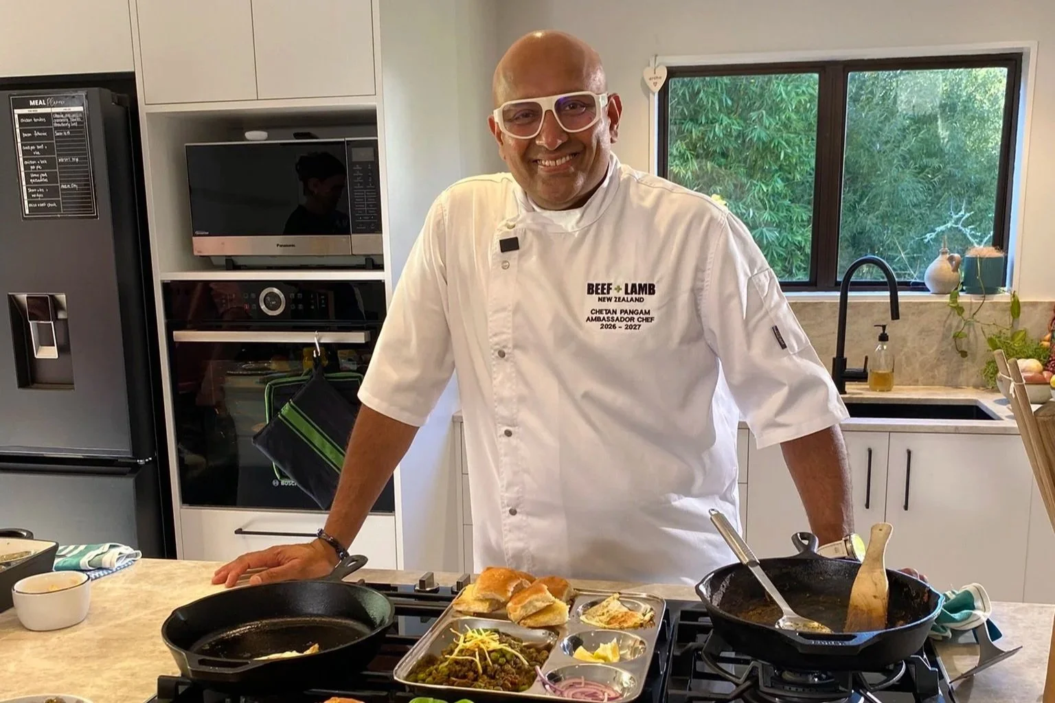Chef wearing a white chefs jacket and cooking keema pav in a domestic kitchen