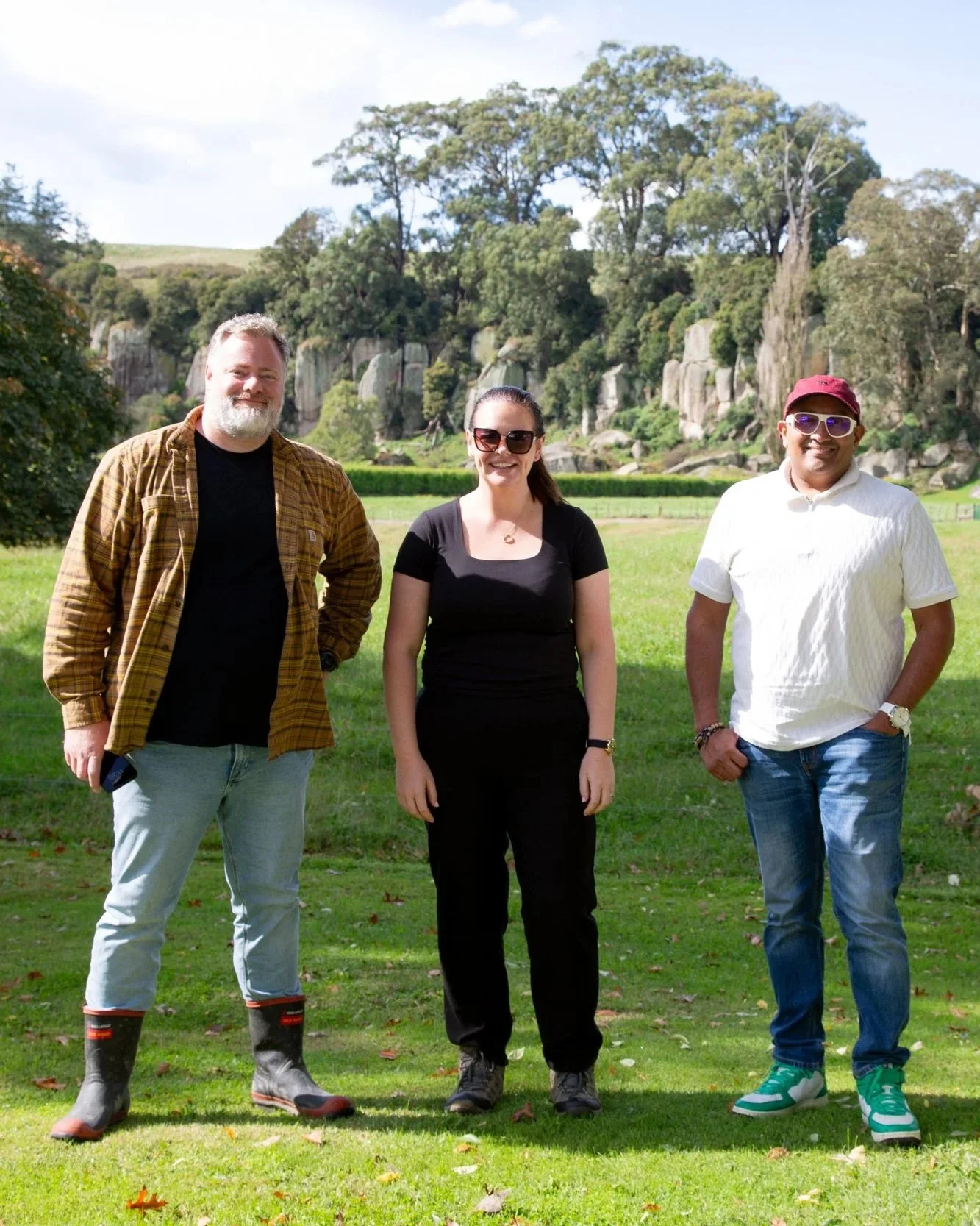 Three people standing in a paddock with rocky bluffs and trees behind