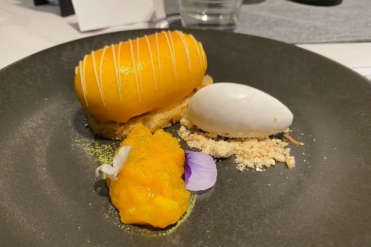 Plated vanilla glazed mango mousse dessert with edible flowers, created by chef Cam Davies