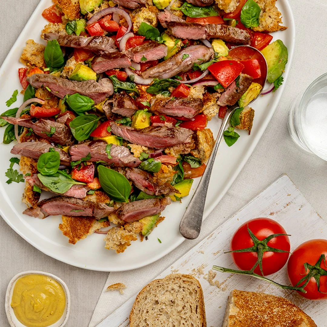 Sliced steak salad with avocado, tomatoes and toasted bread on a white platter