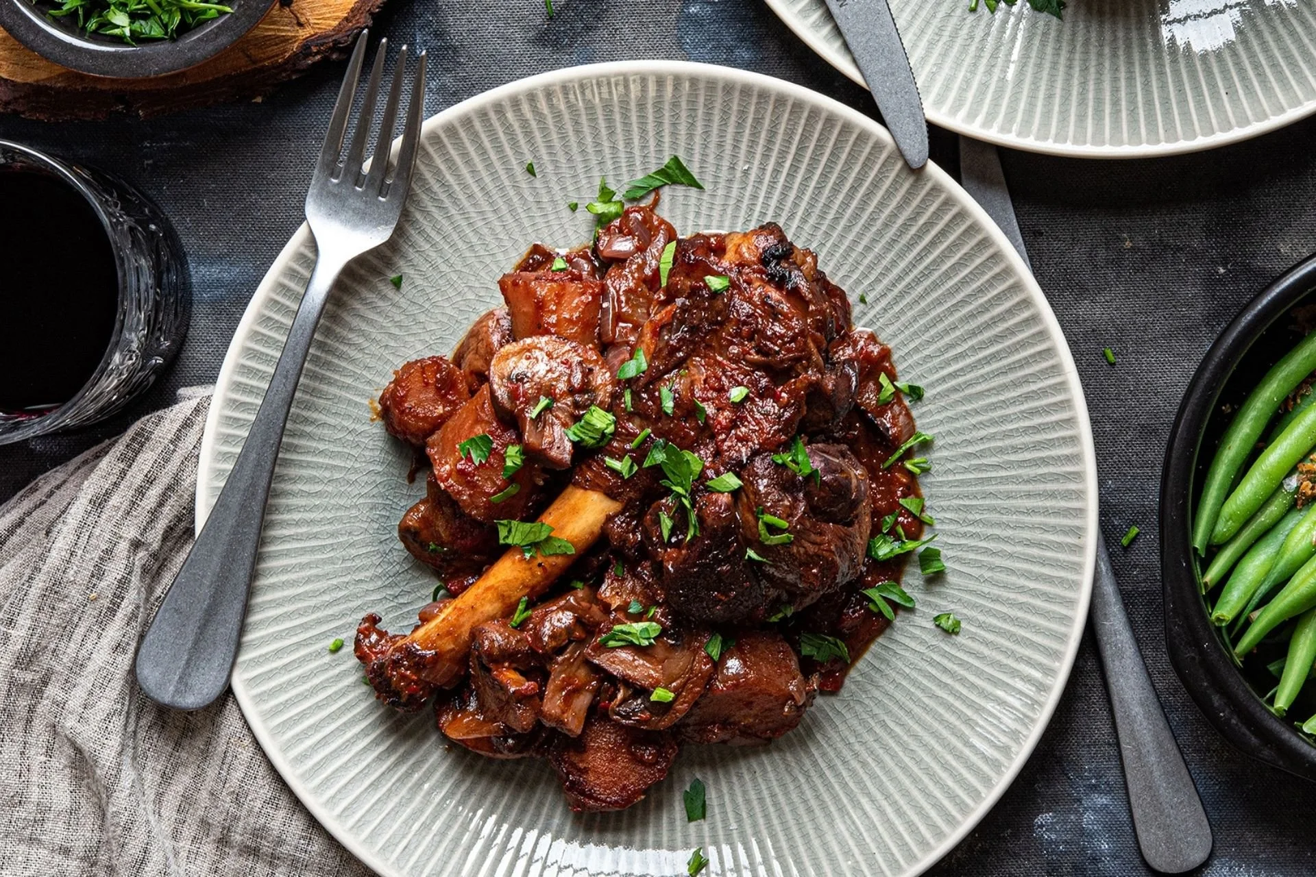 Slow-cooked lamb shanks in a rich, glossy sauce with carrots and fresh parsley, served with green beans.