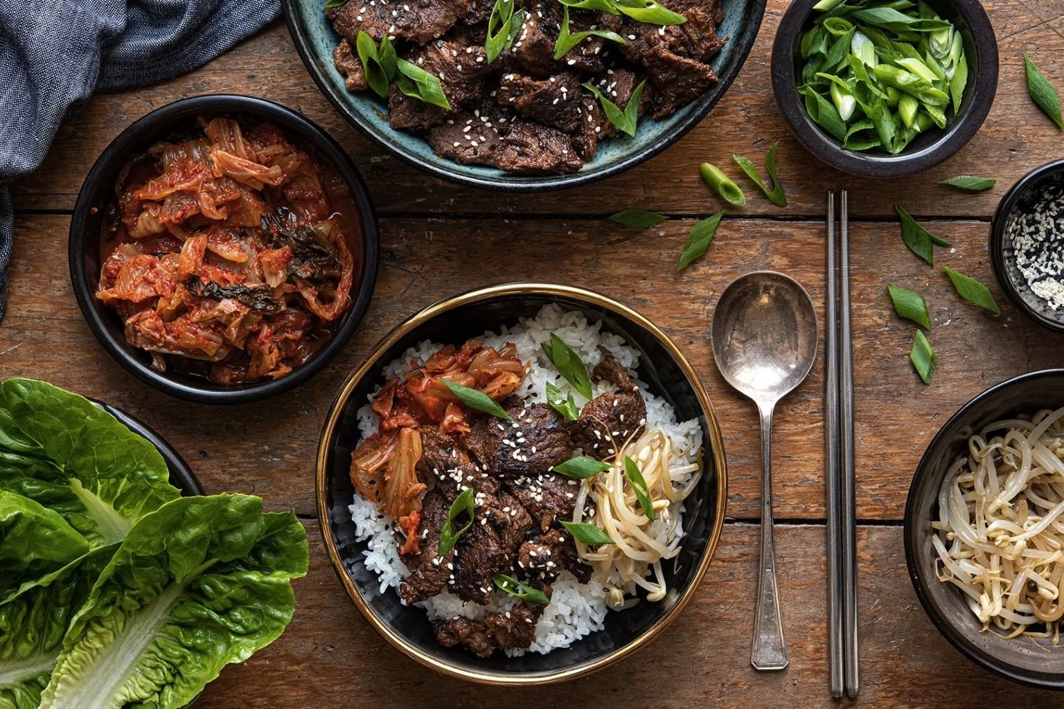 Korean beef bulgogi with rump steak served over white rice with kimchi, bean sprouts and sliced spring onions, sprinkled with sesame seeds.