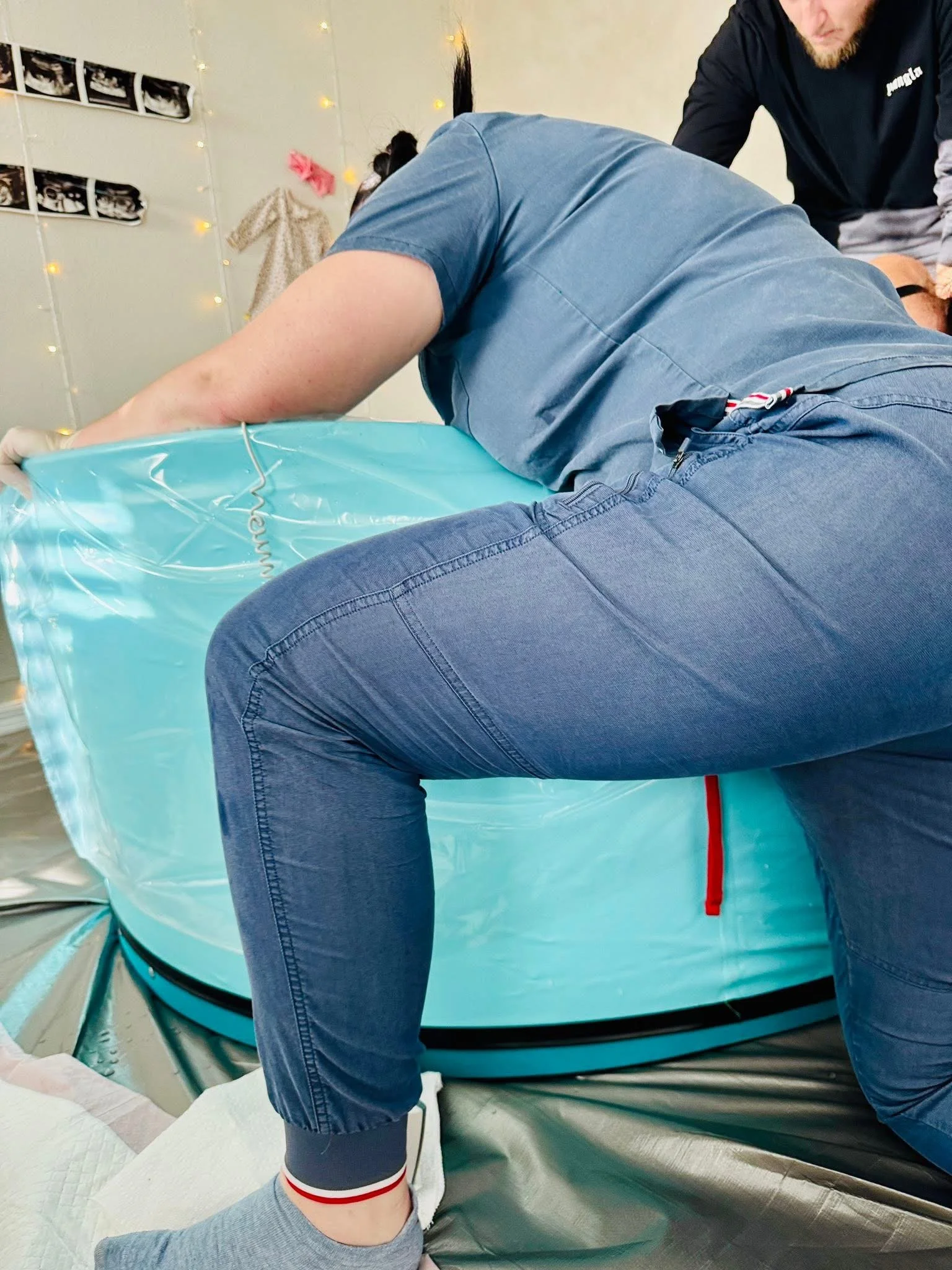 Person lying on a medical table, receiving healthcare treatment from a healthcare professional, in a room decorated with string lights and photos on the wall.
