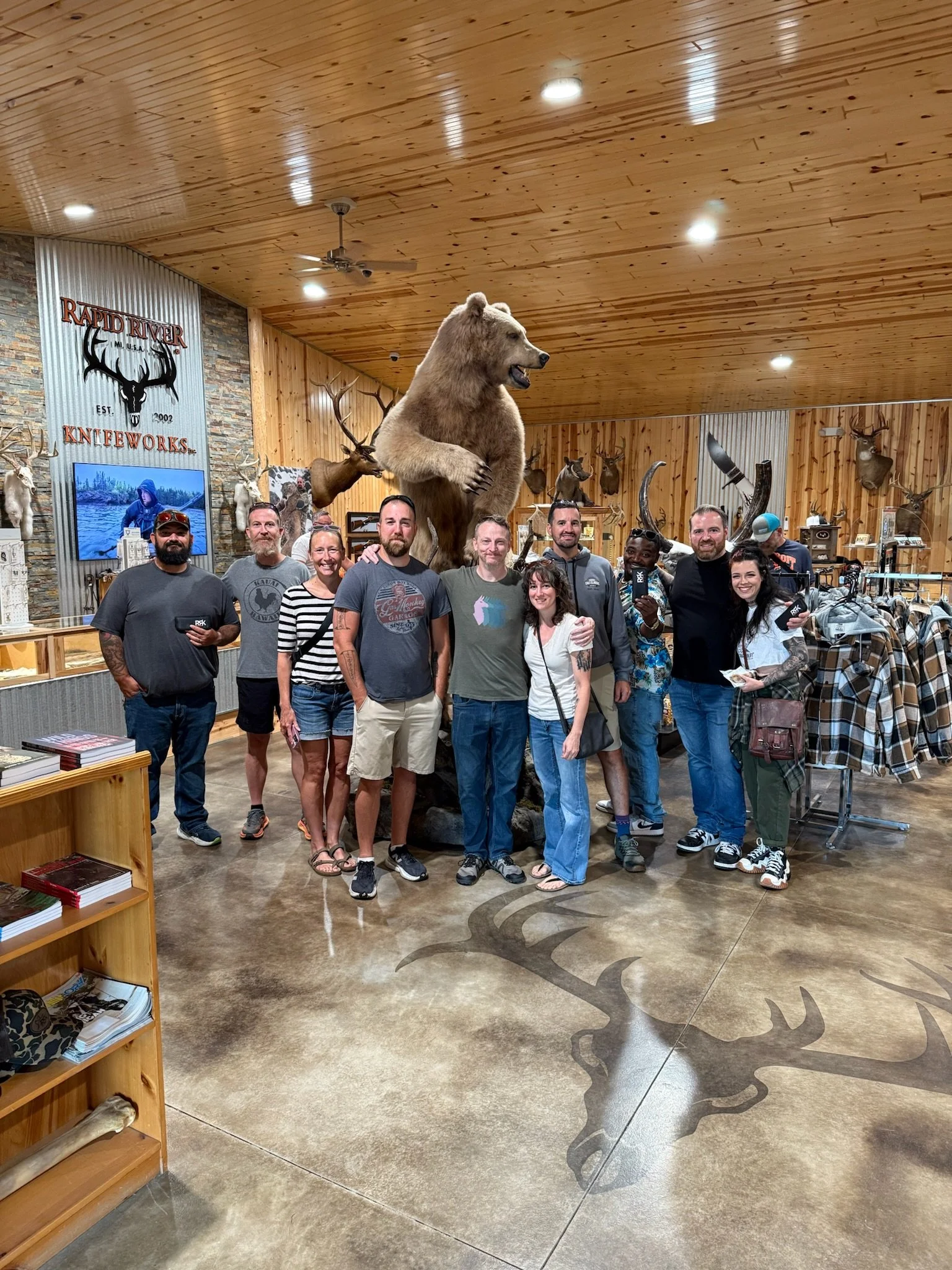 Group of people posing inside a store or lodge with mounted animal heads and a bear statue in the background.