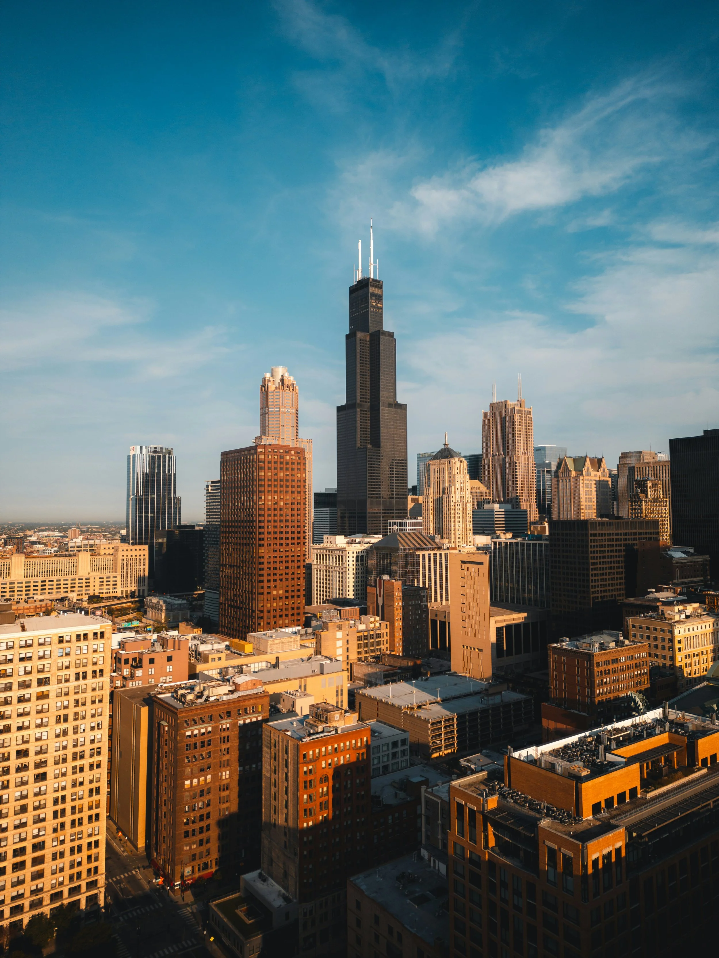 Skyline of Chicago skyline with skyscrapers, including the Willis Tower, under a blue sky with wispy clouds.