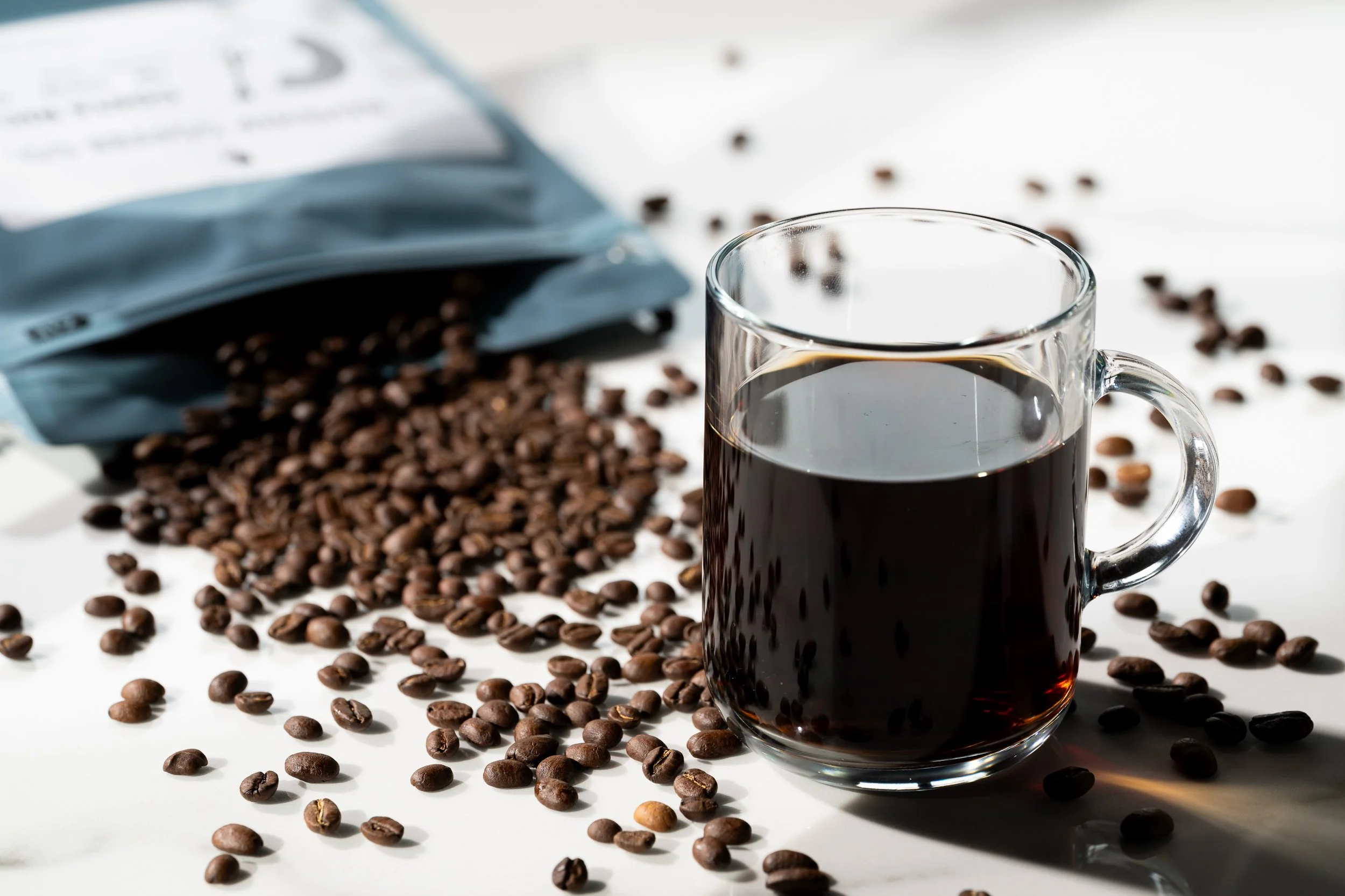 Coffee mug and scattered beans with Kinship Coffee Co bag, specialty coffee product photography
