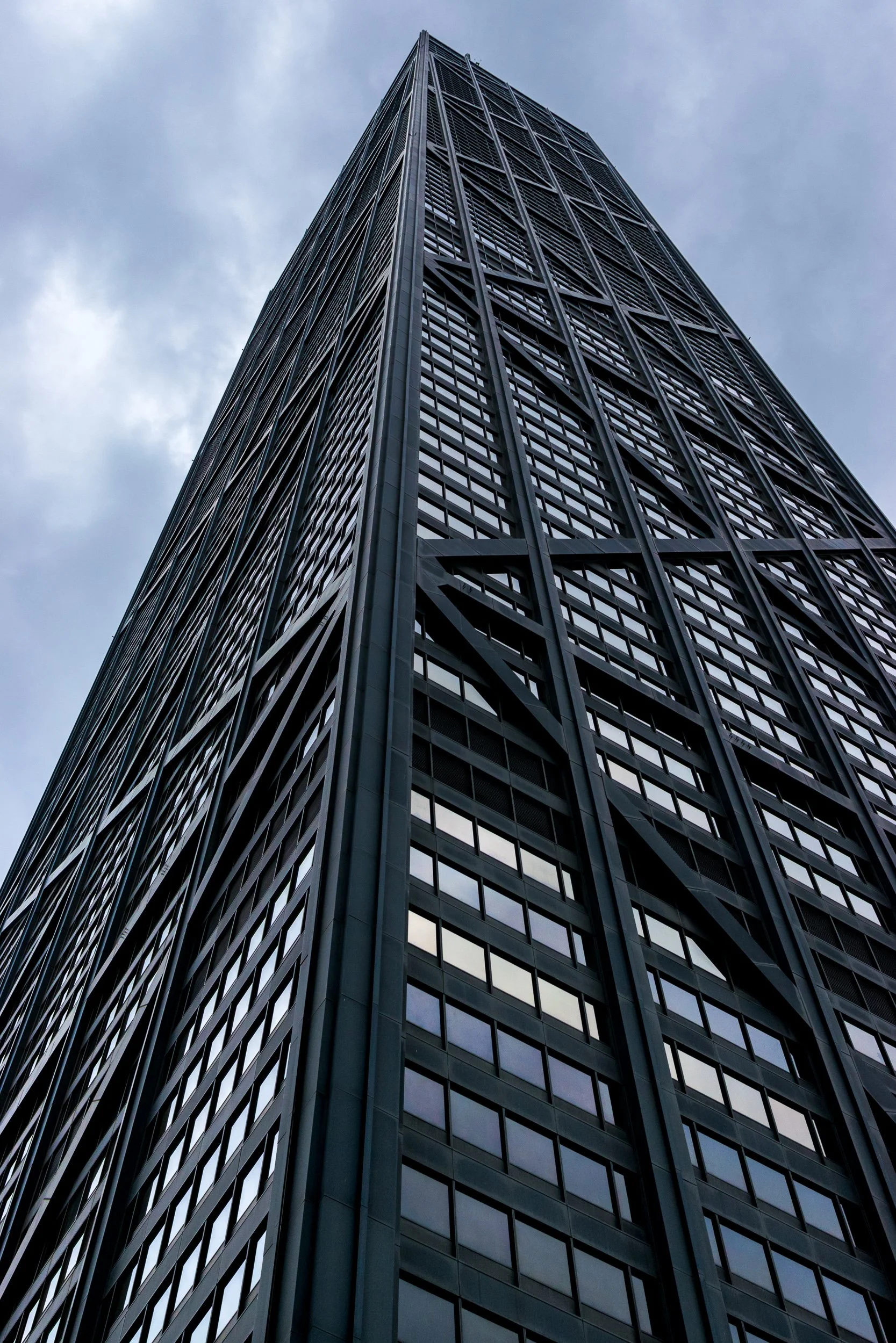 John Hancock Center in Chicago, looking straight up the full height of the tower, diagonal steel cross-bracing against an overcast sky.