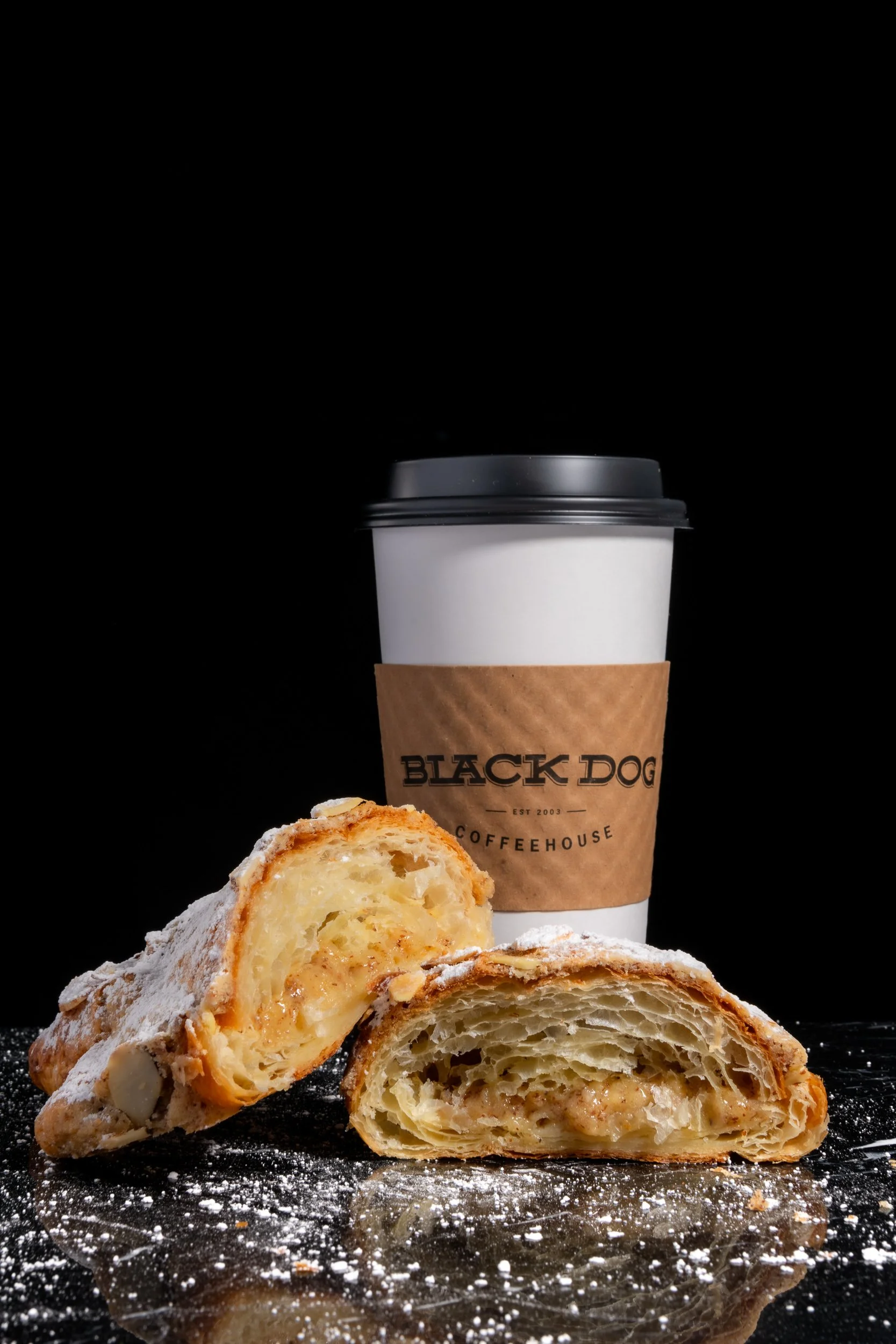 Black Dog Coffeehouse cup and split pastry on black surface, Kansas City coffee shop brand photography
