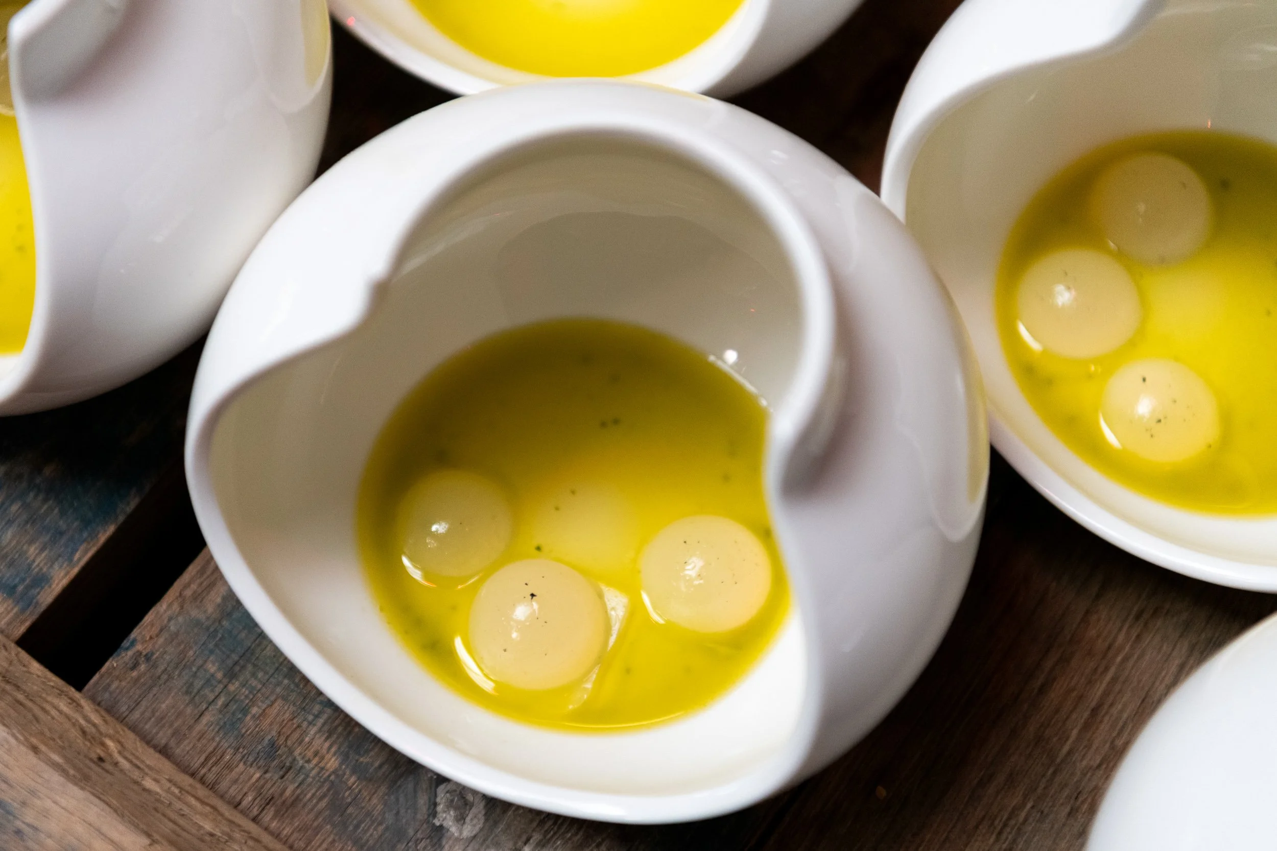 Raw egg yolks in cracked white ceramic vessels, fine dining ingredient photography
