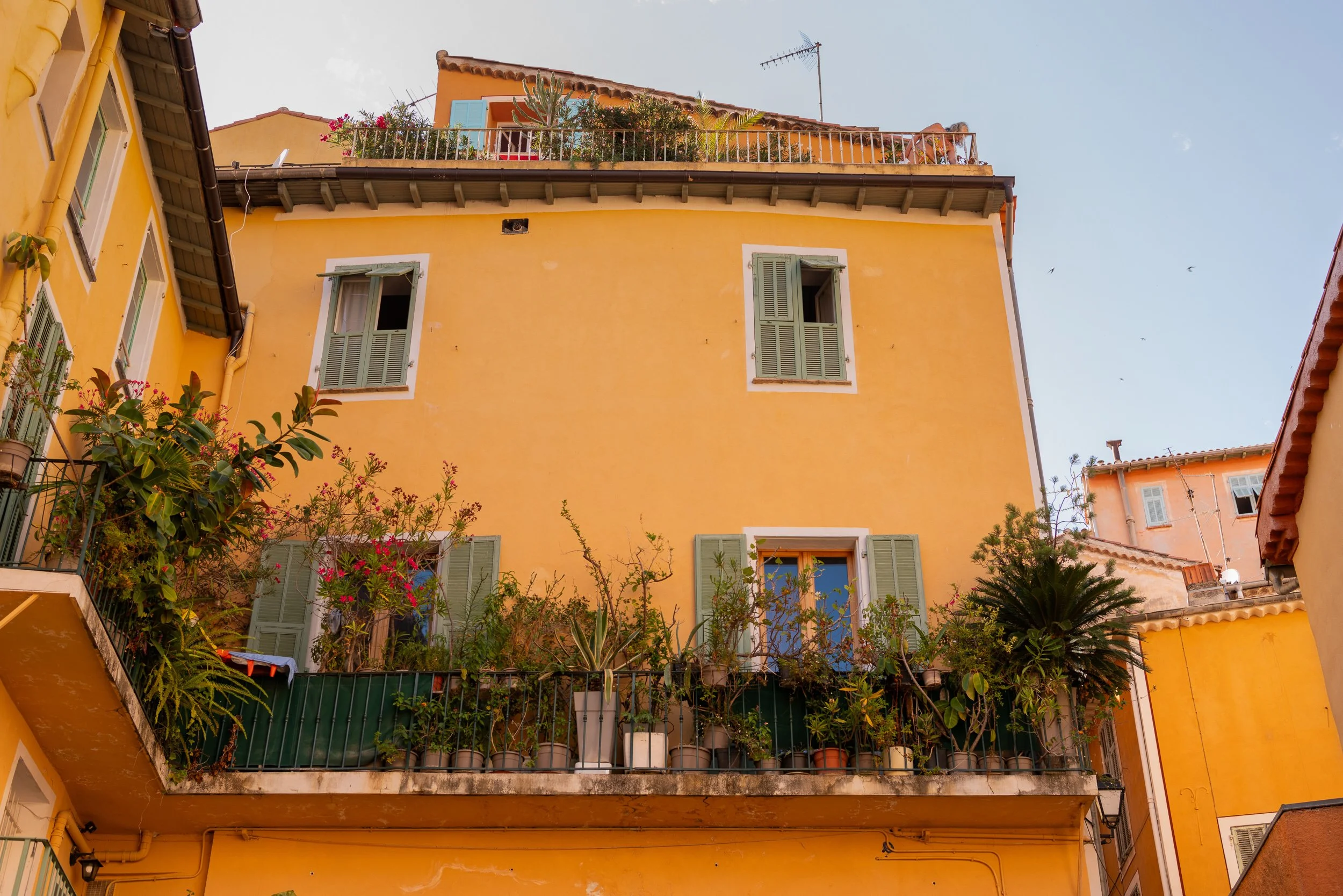 Orange-painted building facade with window shutters and plants cascading from balconies, French Riviera.