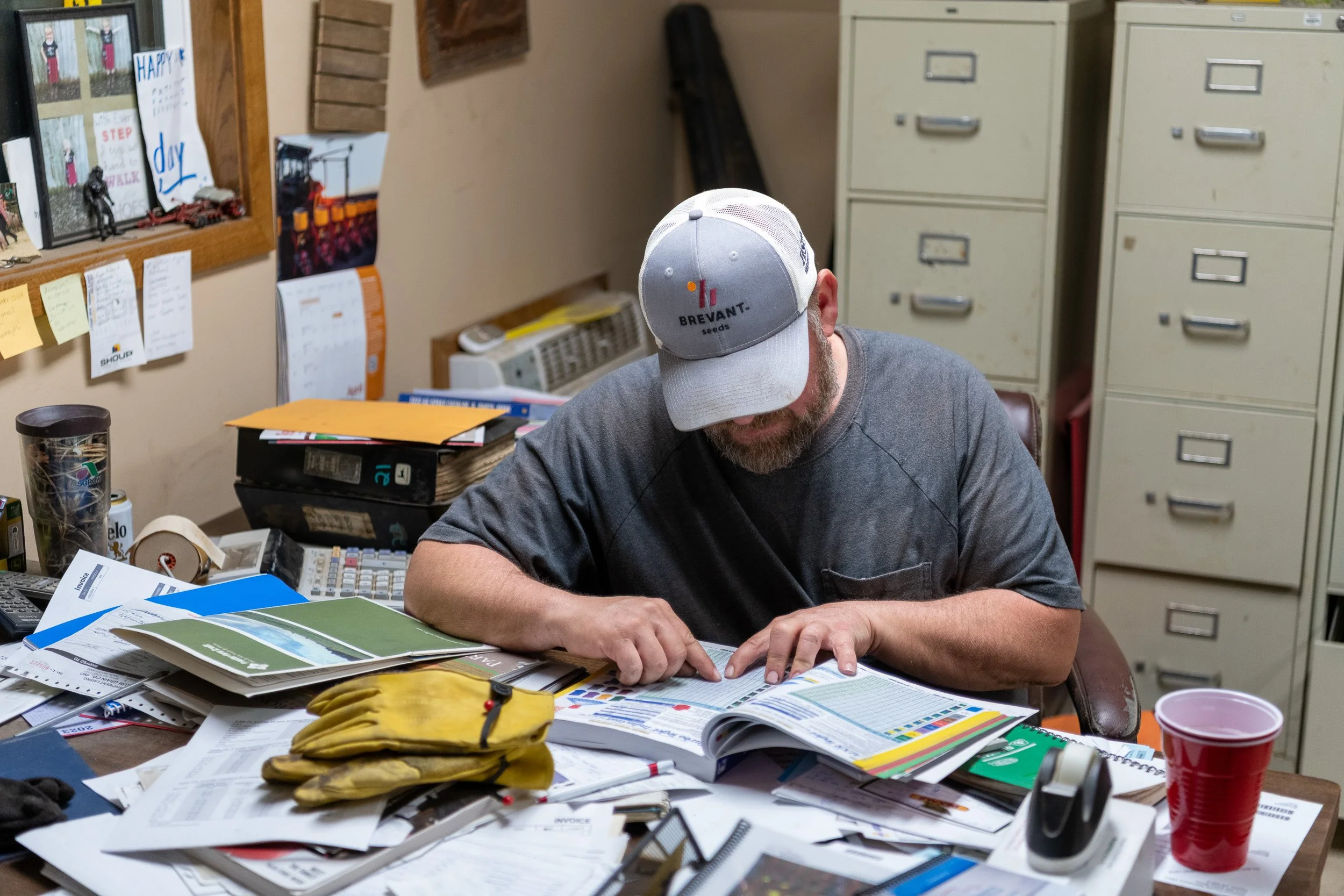 Farmer reviewing records at a desk covered with paperwork and maps.