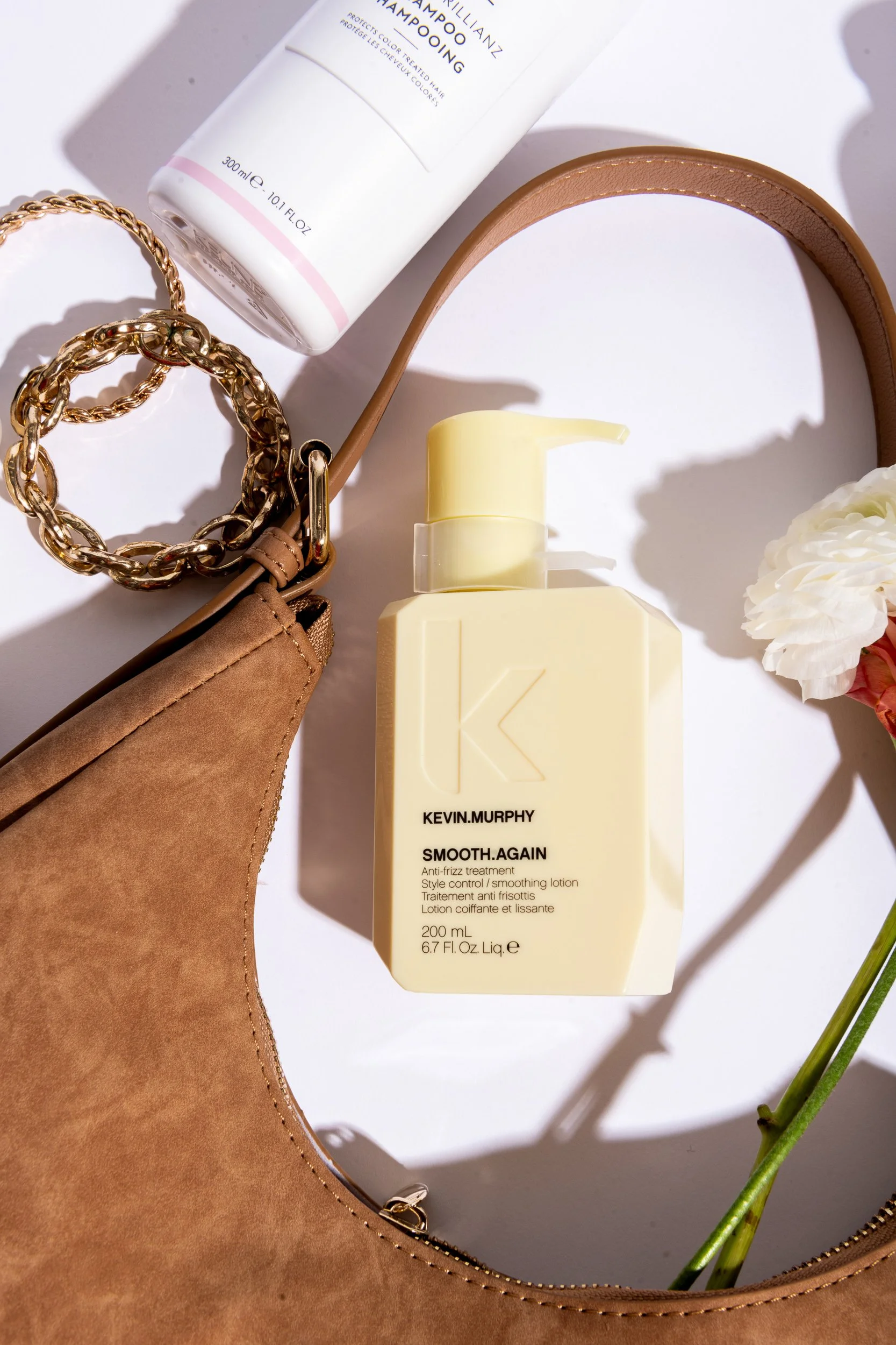 Kevin Murphy Smooth Again hair product styled with a suede bag, gold chain, and flower