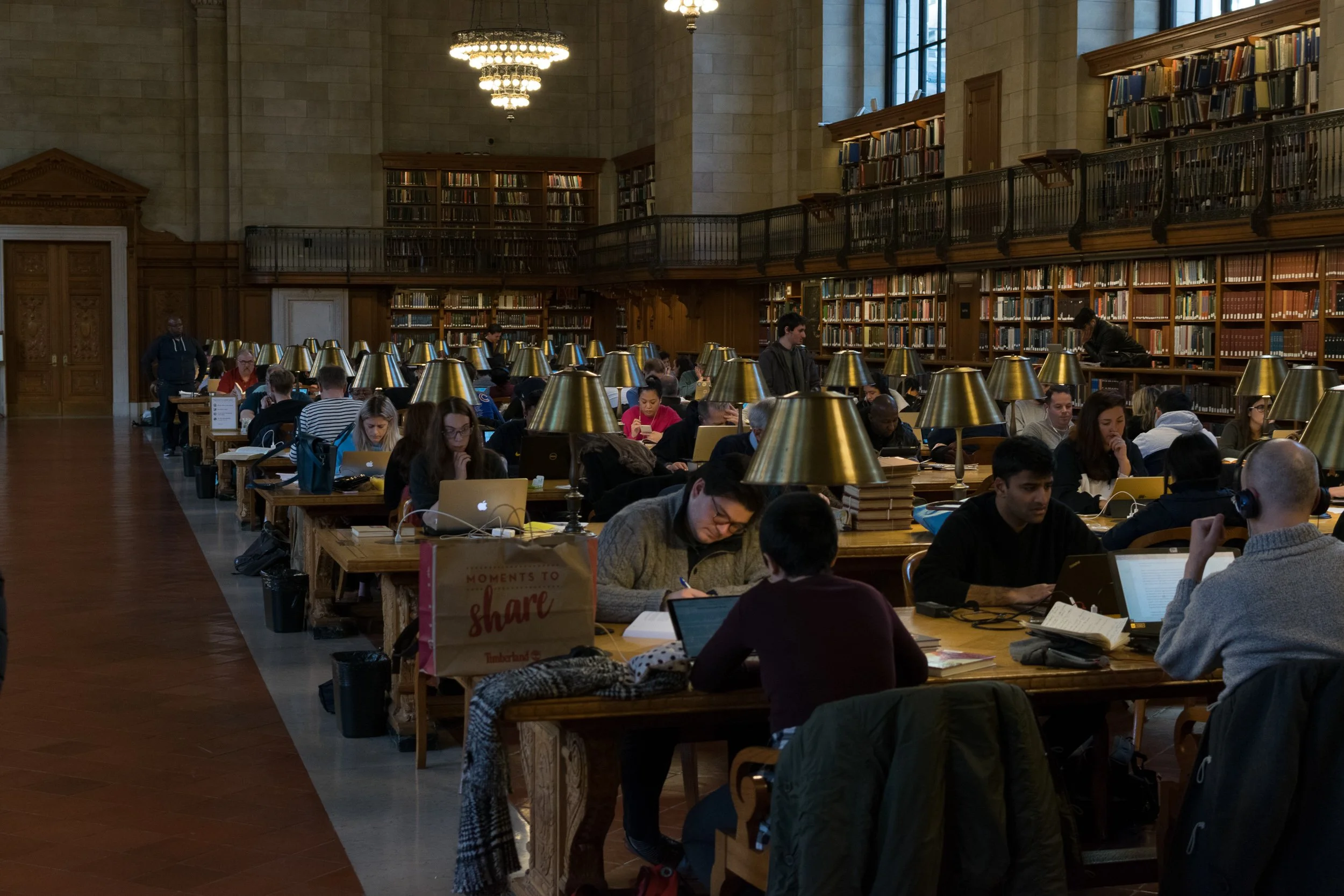 New York Public Library main reading room, warm brass lamps over long rows of researchers at wooden tables.