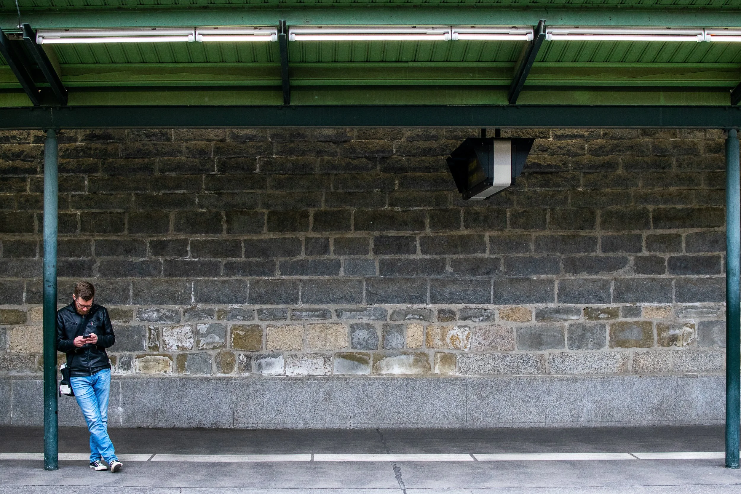 Bratislava train station interior, lone figure standing at a stone shelter against a massive old stone wall.
