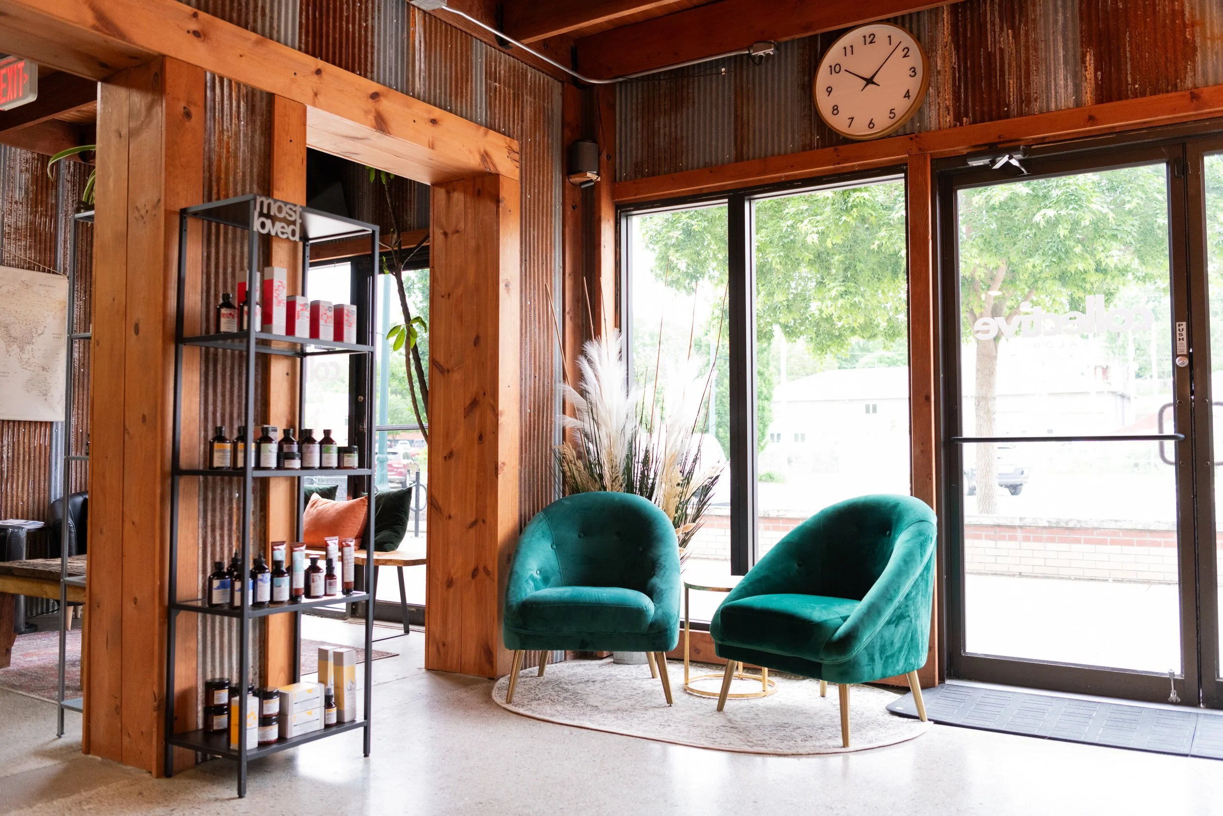 Salon waiting area with teal velvet chairs, product shelving, and large windows