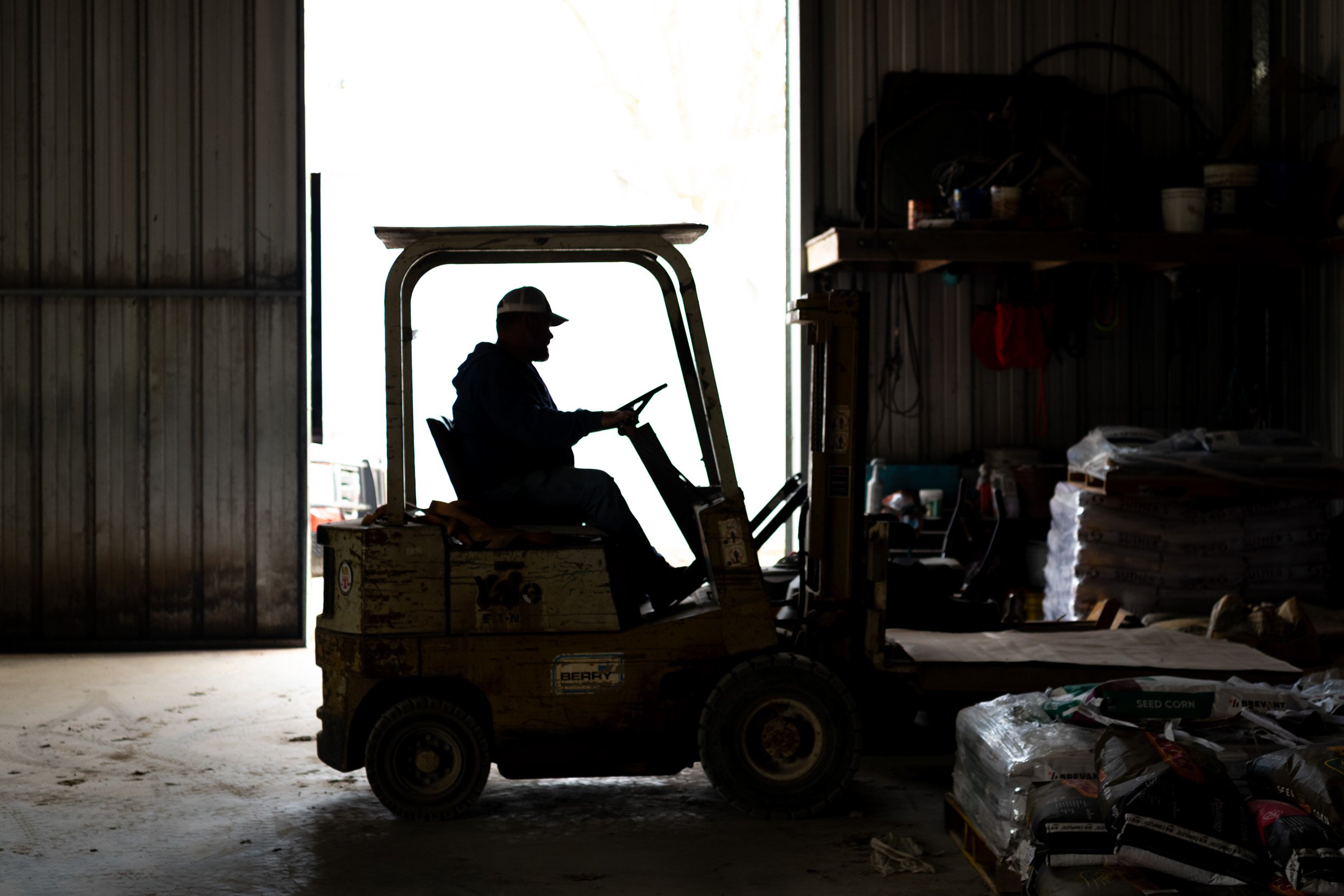 Farmer driving a forklift inside a farm equipment shed.