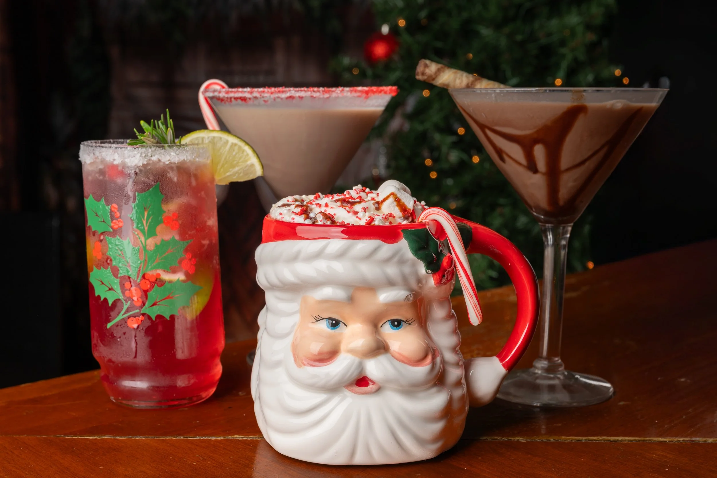 Three holiday cocktails on wood bar including Santa mug and martinis, seasonal restaurant menu photography
