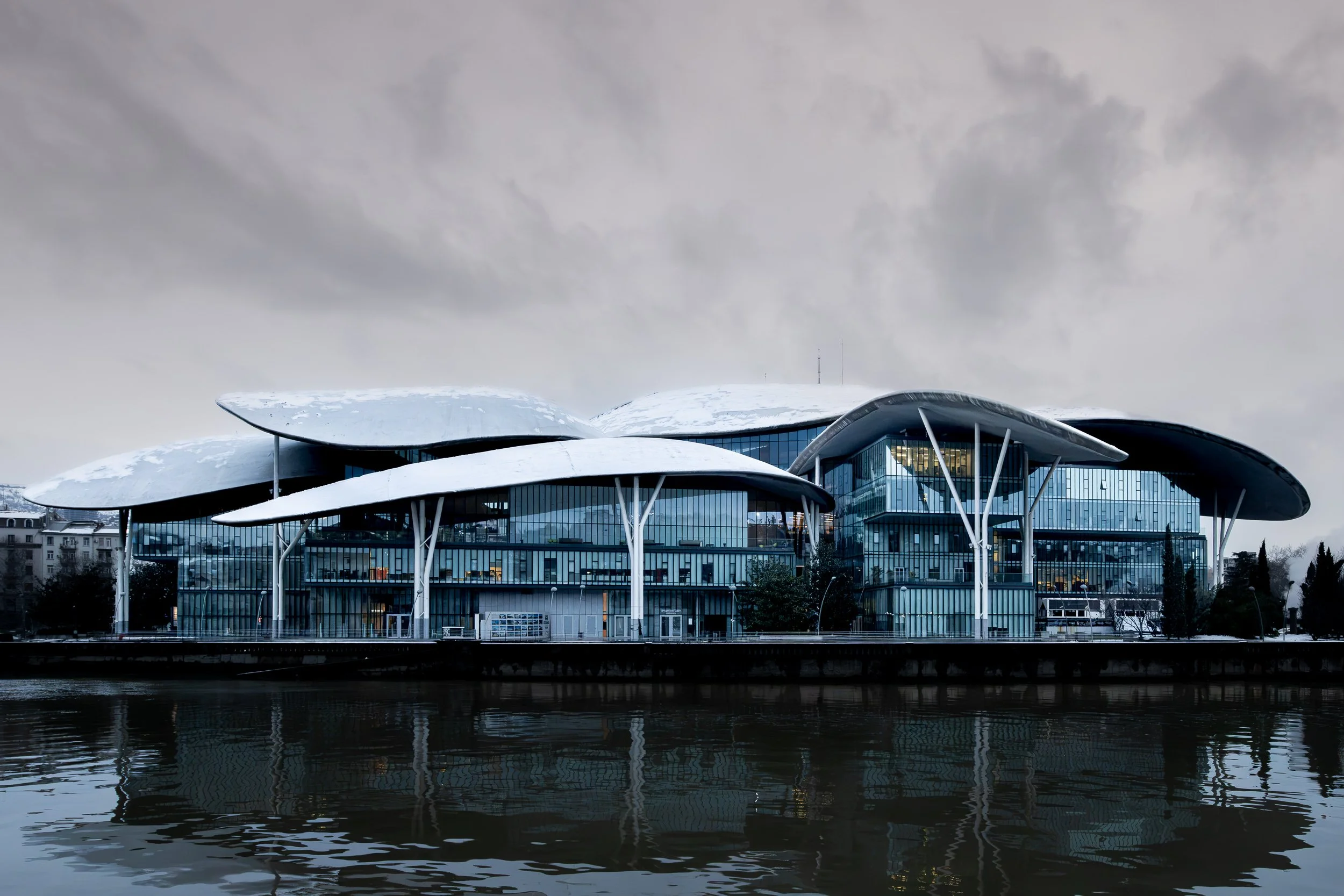 Contemporary architecture reflects across the river, contrasting clean geometric lines with an overcast winter sky.