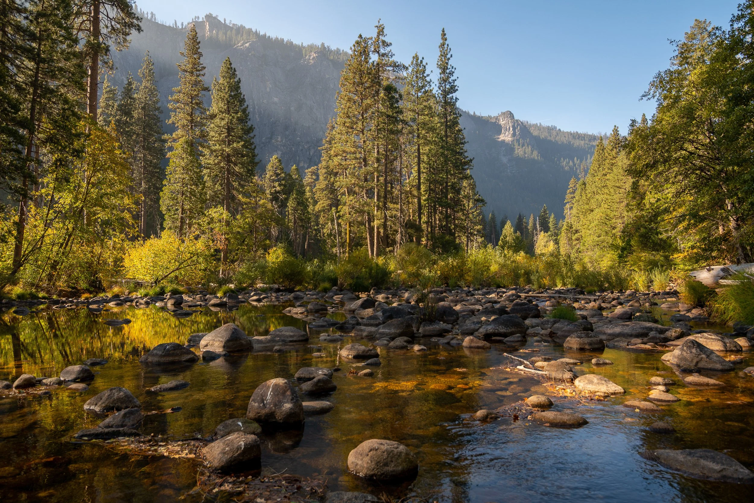Yosemite Valley, Merced River in the foreground with boulders and fall foliage, granite valley walls behind.