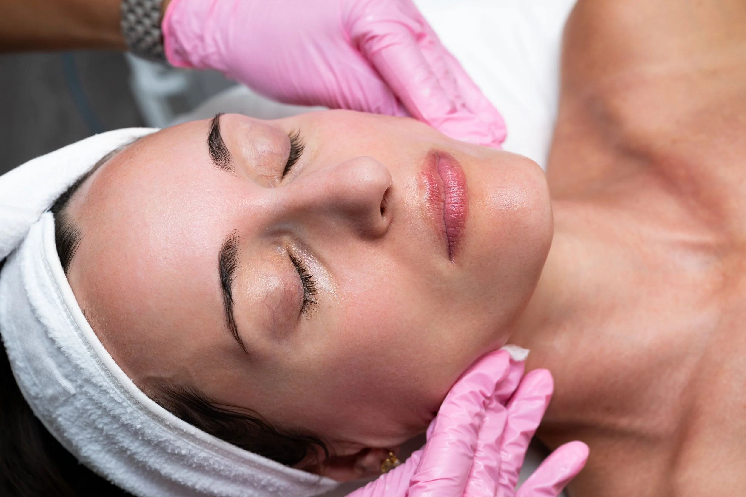 Woman receiving a facial treatment with pink-gloved hands working on her skin