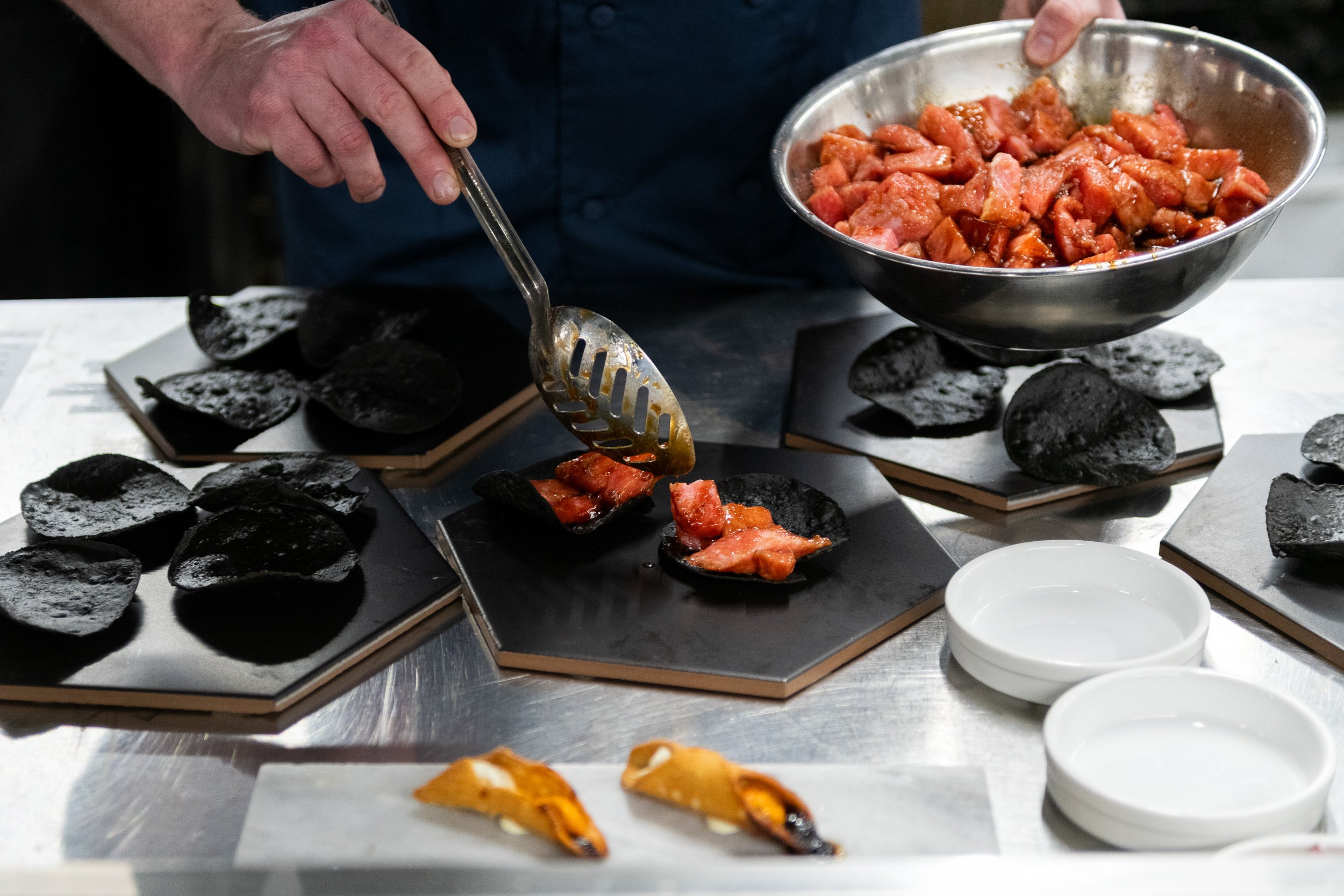 Chef plating lobster onto black hexagonal boards with tongs, fine dining kitchen preparation
