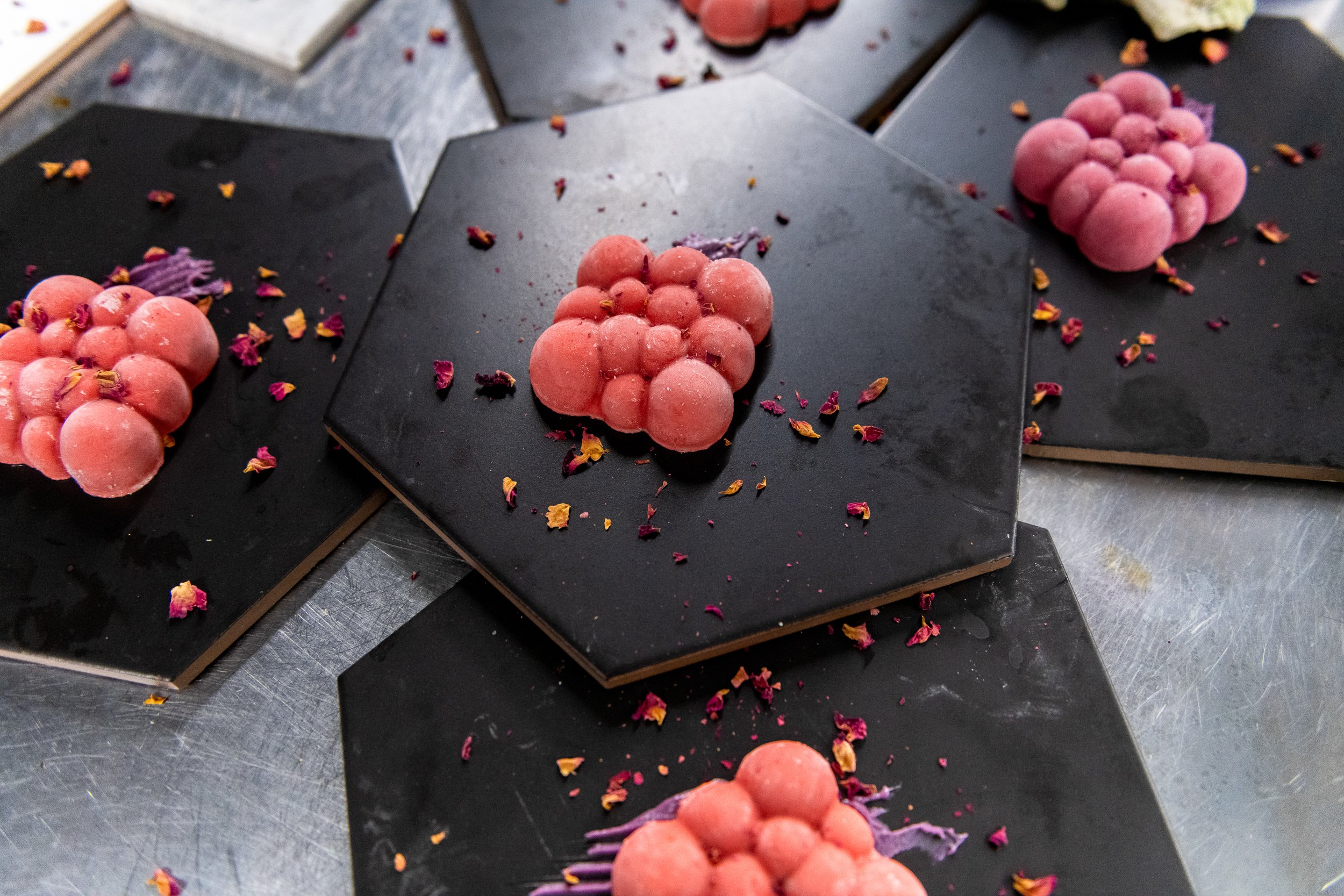 Rose pink spherical desserts on matte black hexagonal plates with dried flower petals
