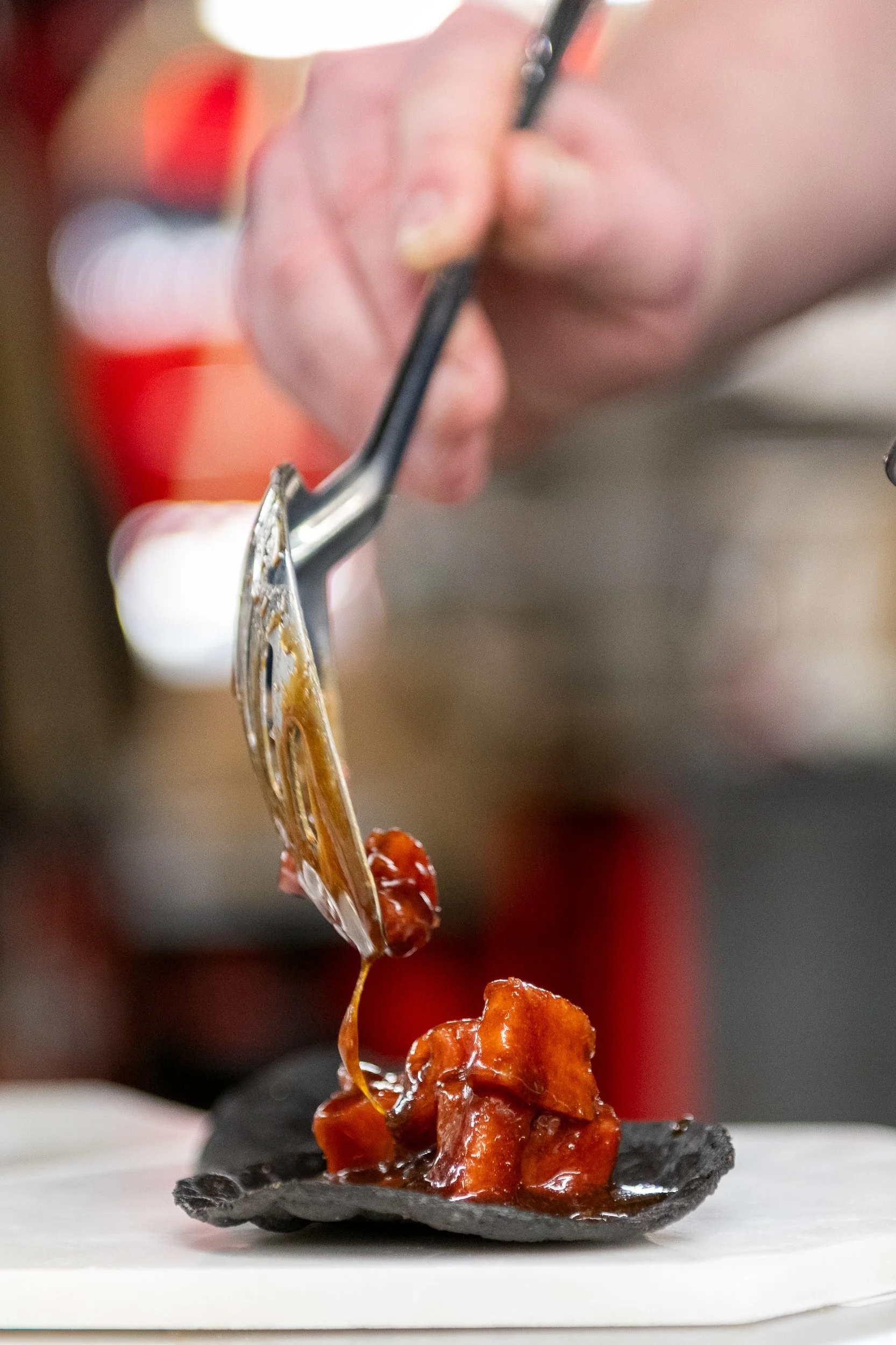 Chef ladling braised protein during kitchen dinner service, restaurant food photography
