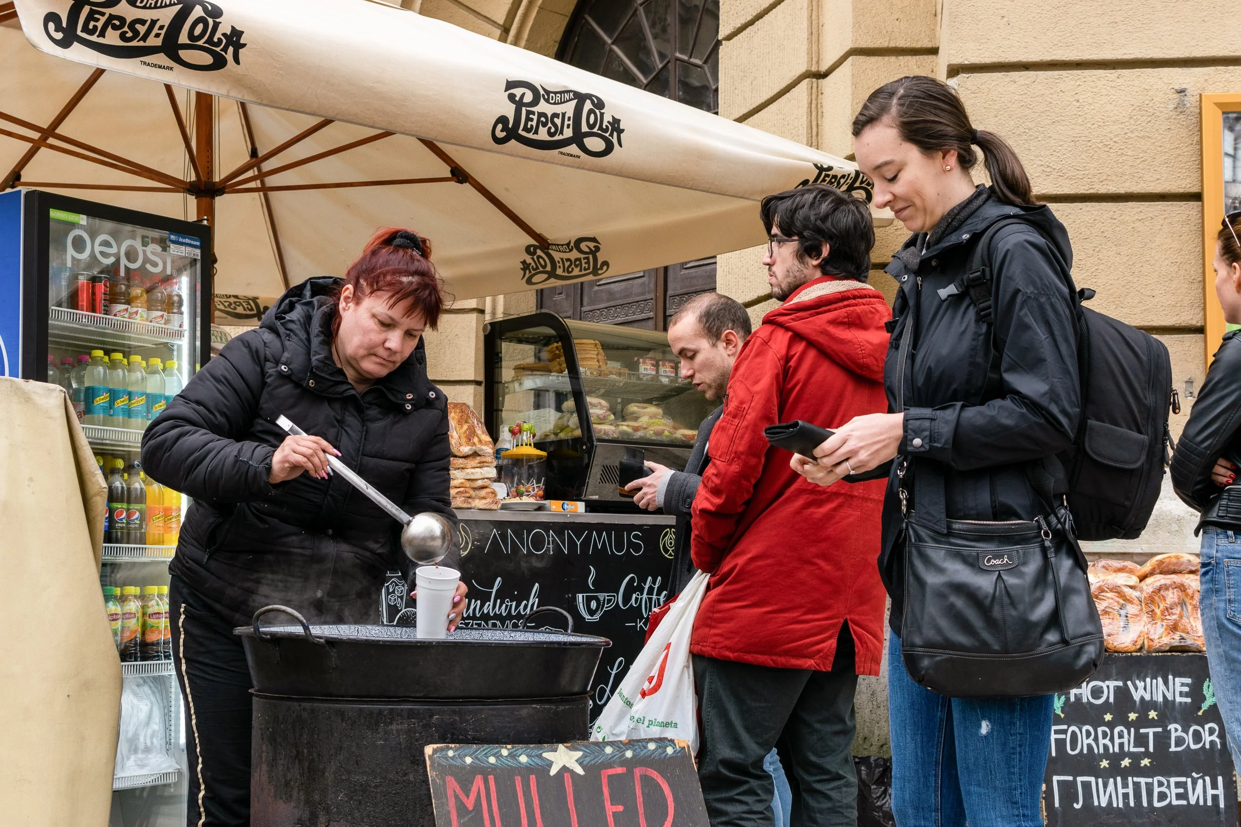 Budapest Christmas market food vendor serving mulled wine, people in winter coats.