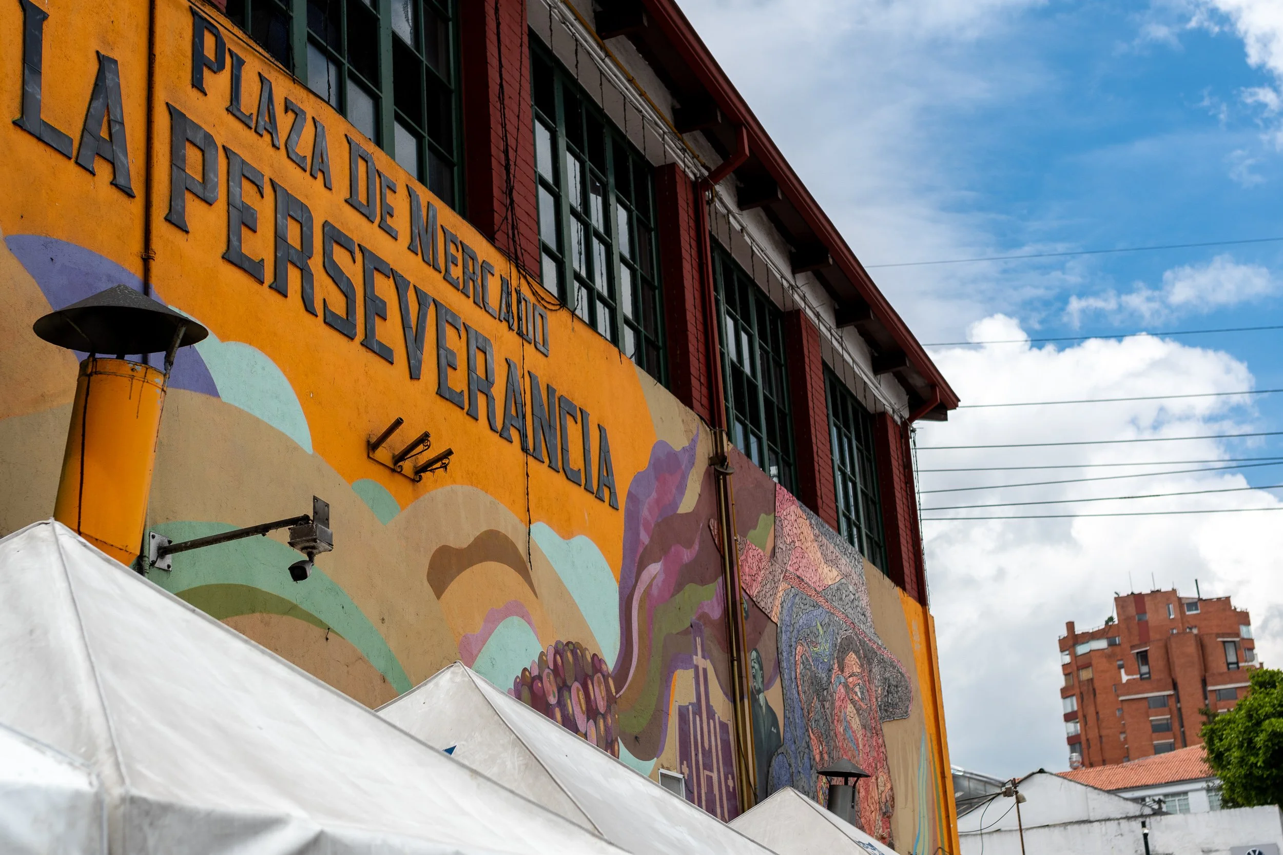 La Perseverancia market building with vivid orange and red painted facade and bold Spanish text, Bogota.