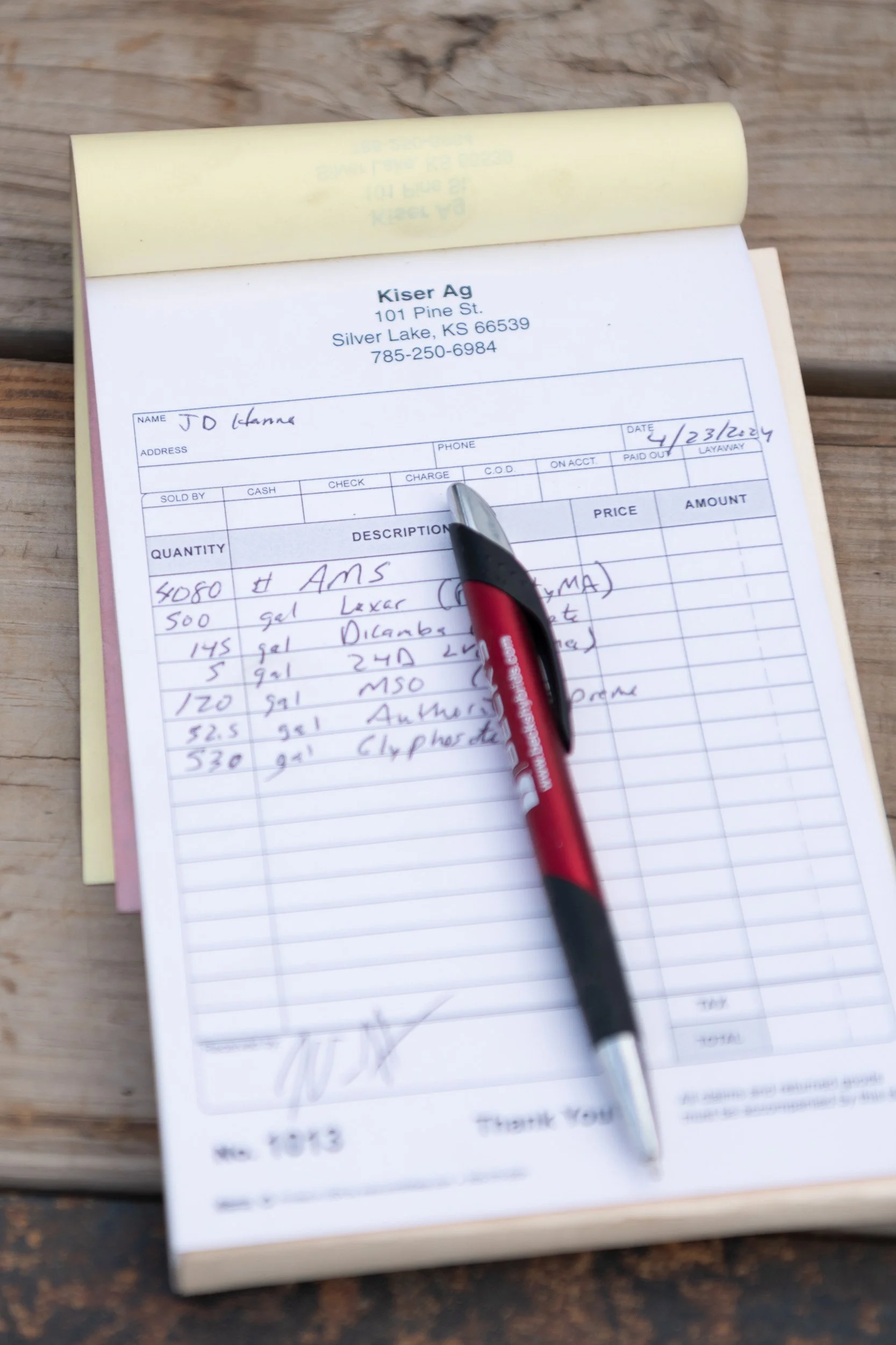 Handwritten farm supply list on a notepad beside a pen.
