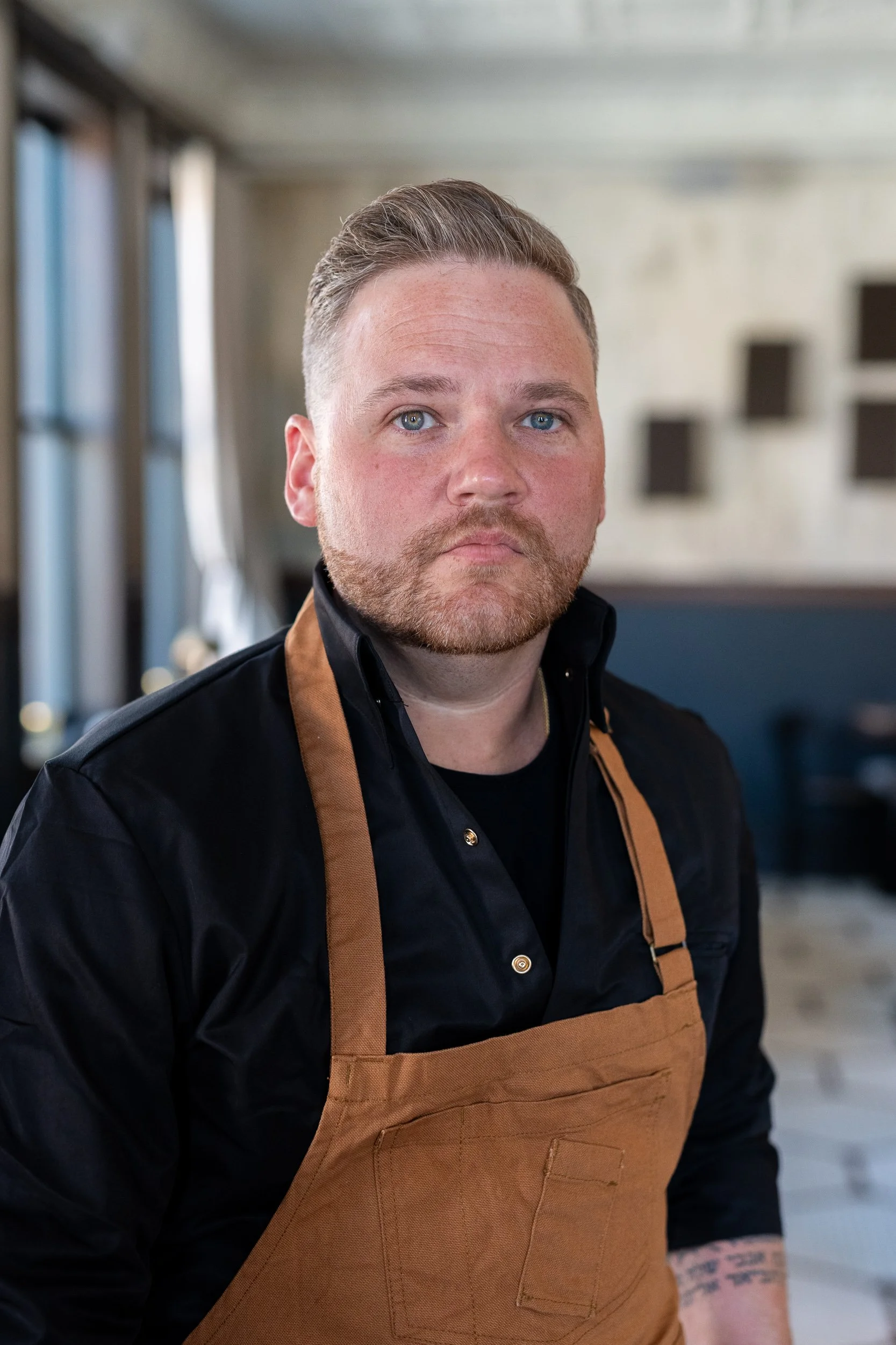 Chef in brown leather apron looking directly at camera in a restaurant interior
