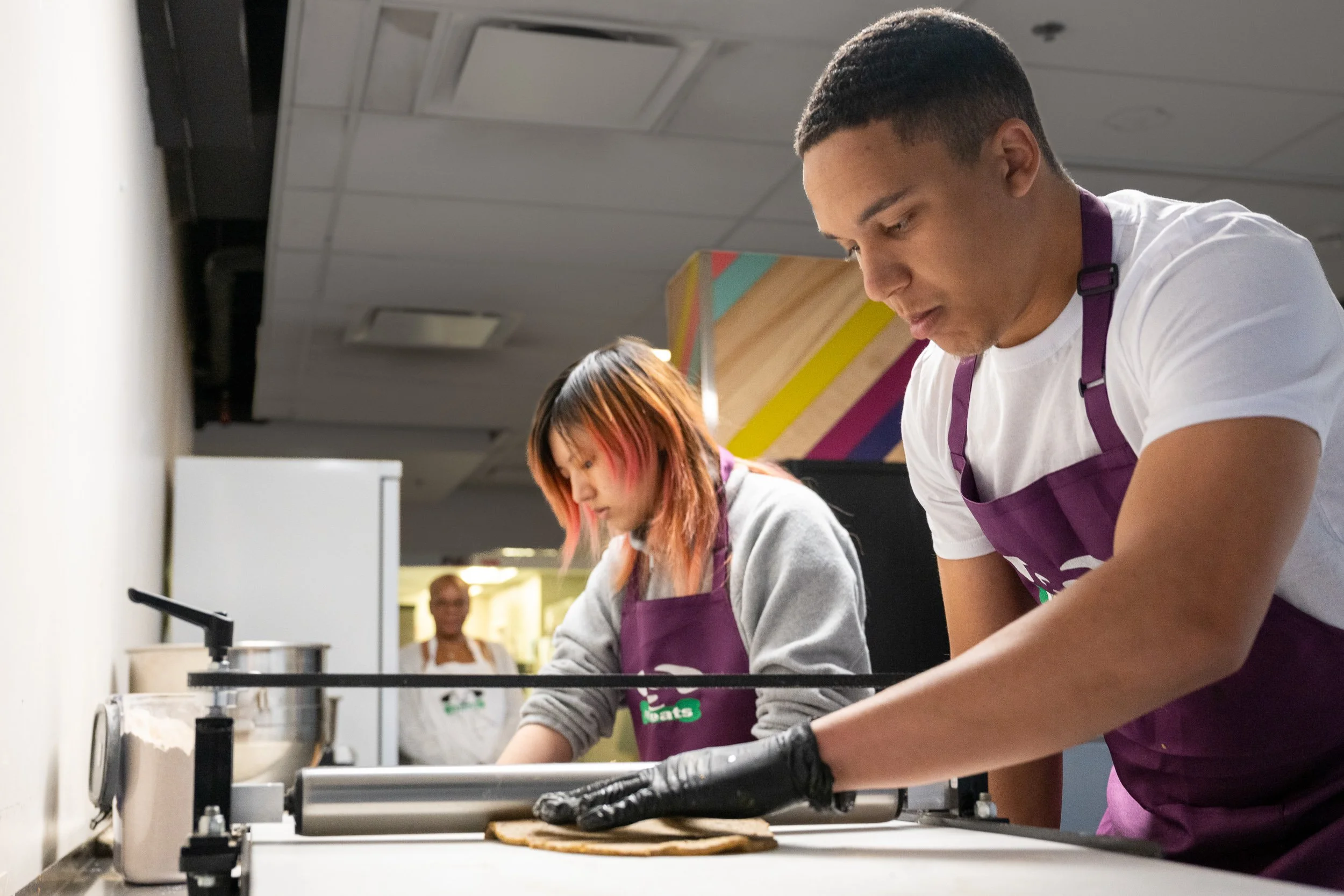 Two workers in purple aprons preparing food at a commercial kitchen counter