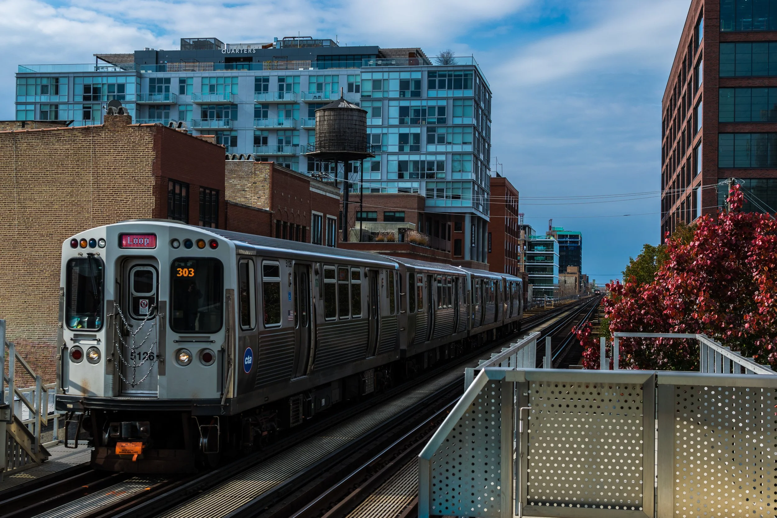 CTA Red Line train arriving at an elevated station in Chicago with autumn trees in the background.