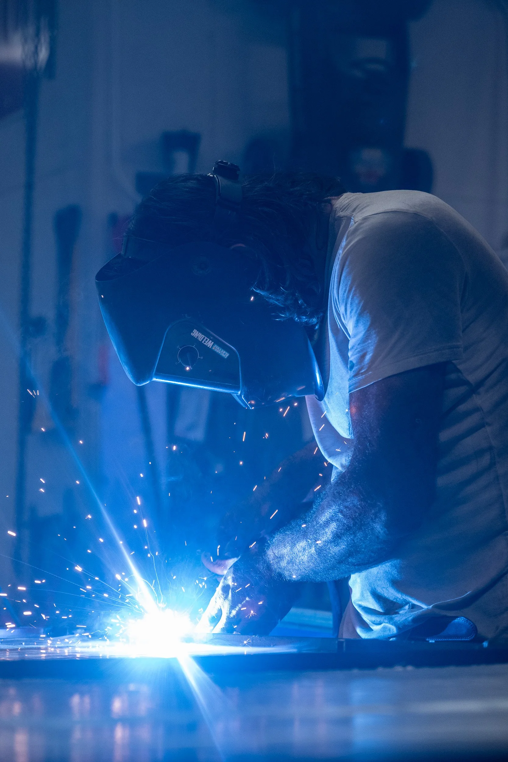 Welder silhouetted against the bright blue arc of a torch, sparks scattering in the dark
