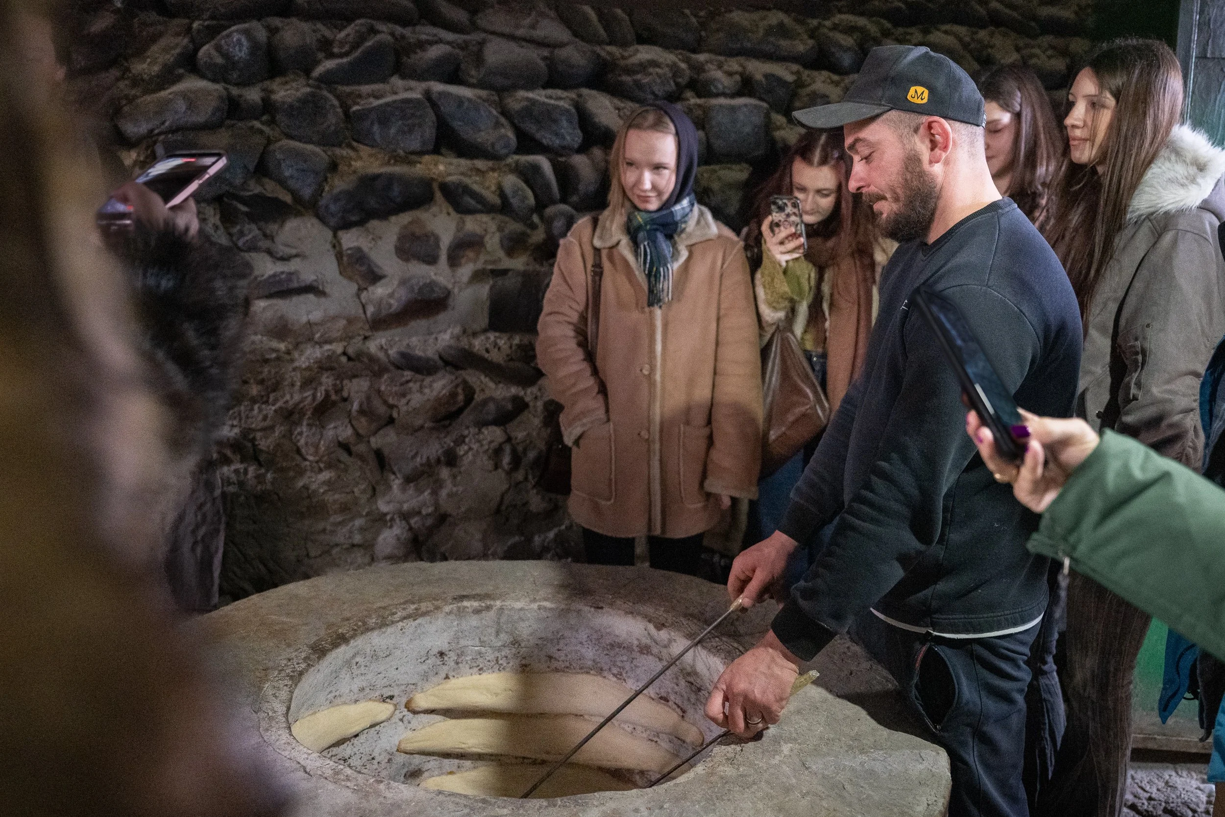 A baker pulls fresh bread from a traditional oven while visitors watch a craft practiced for generations.