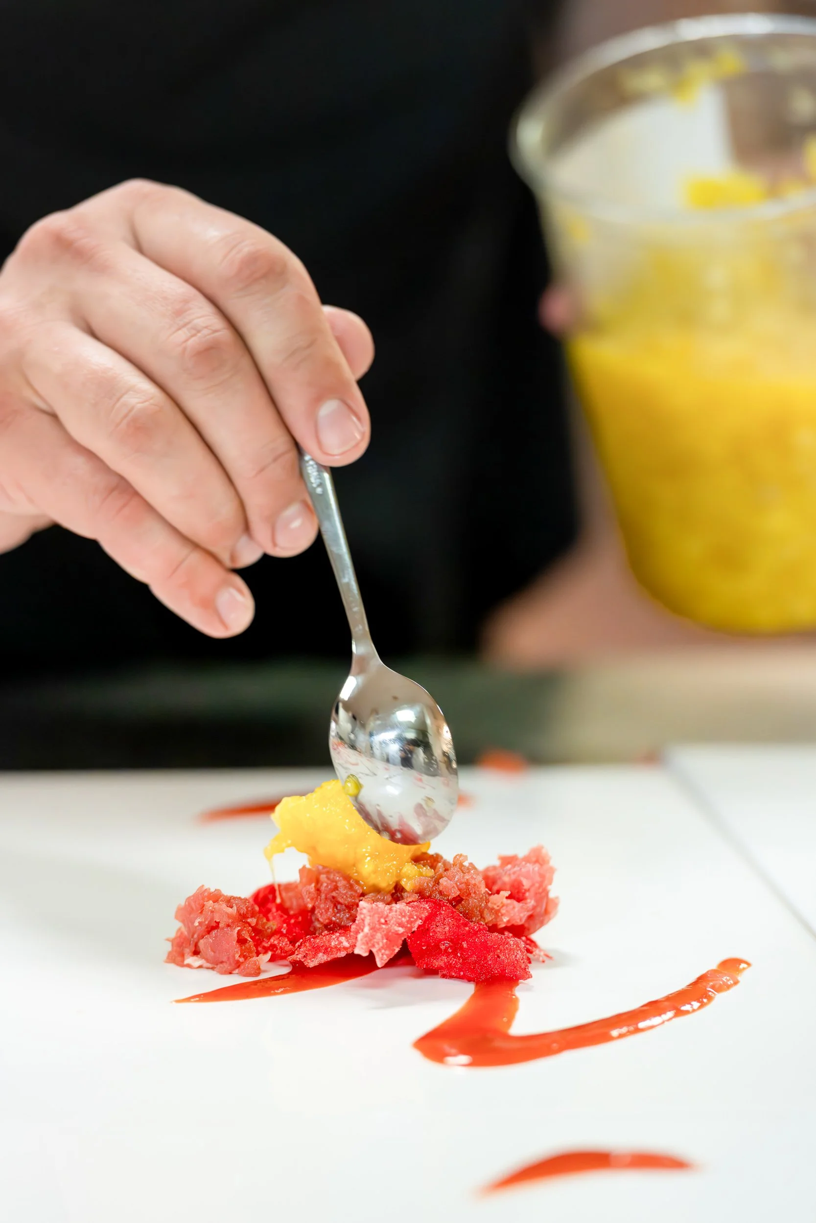 Chef spooning mango onto tuna tartare during fine dining plating service
