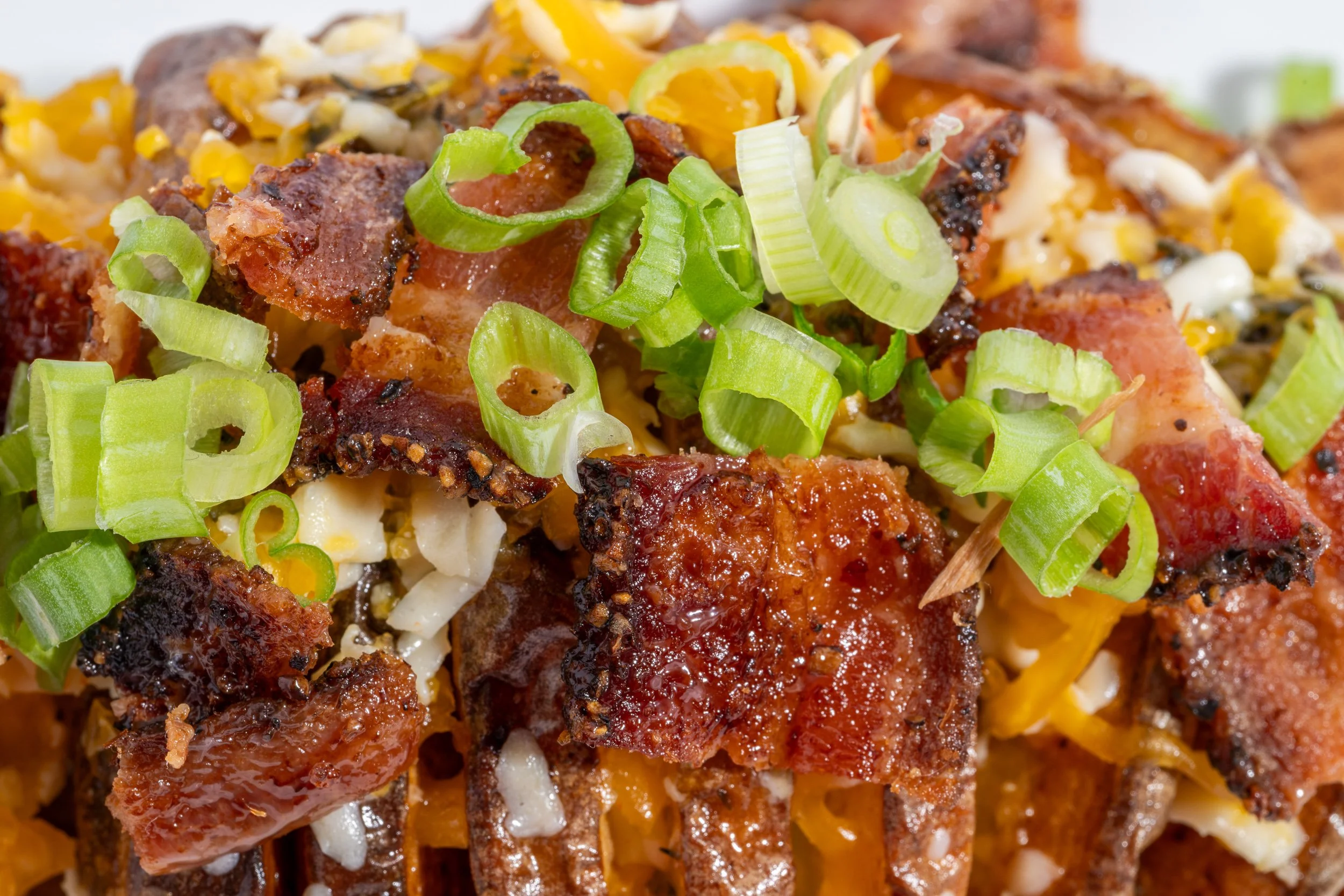 Loaded potato dish with bacon cheddar and green onion close up, brewery menu food photography
