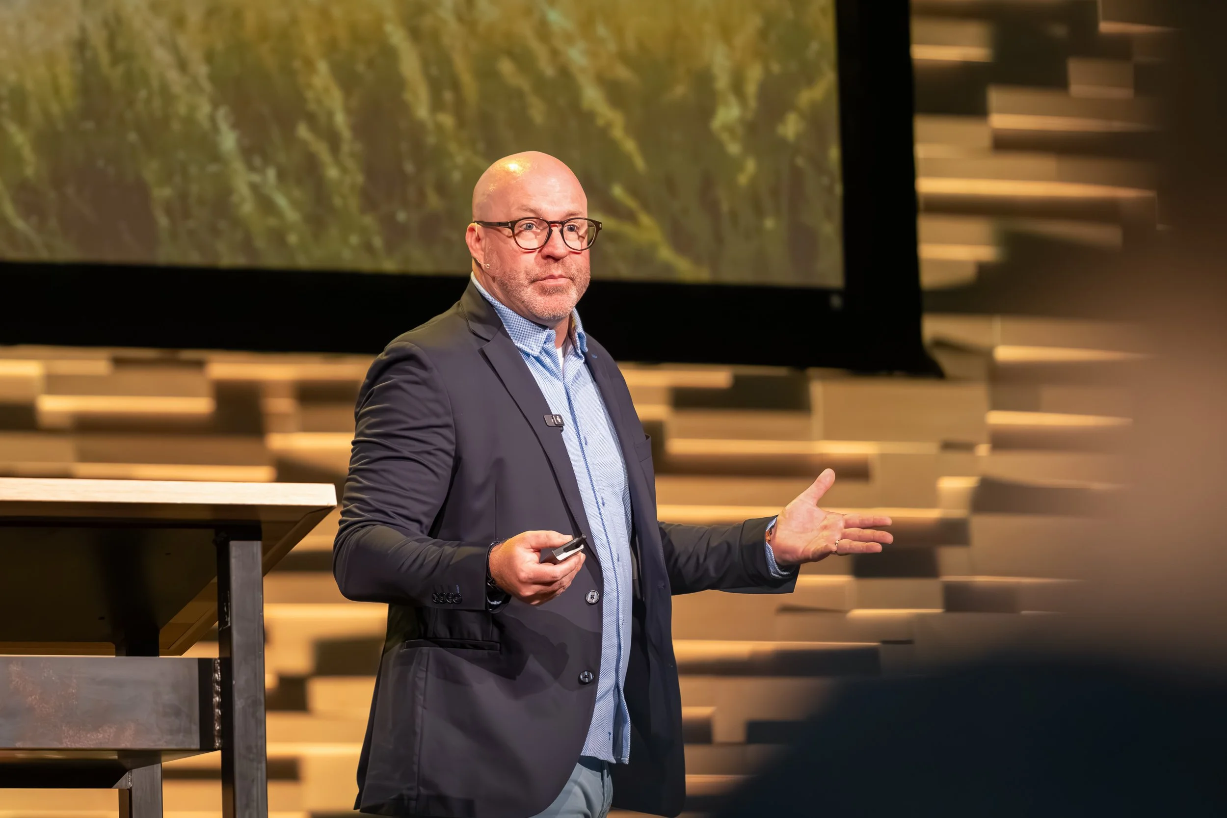Keynote Speaker in blazer gesturing on a stage with a large projected image behind him